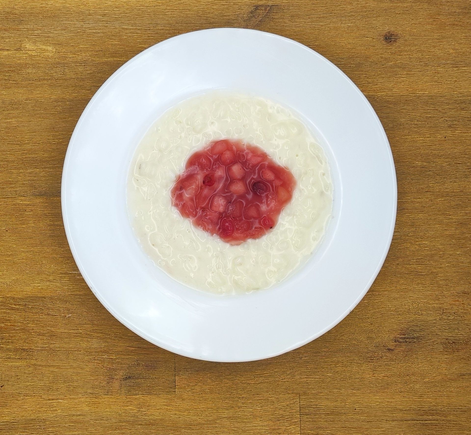 Haferflocken mit roter Marmelade in der Mitte, auf einem weißen Teller, der auf einem Holztisch steht.