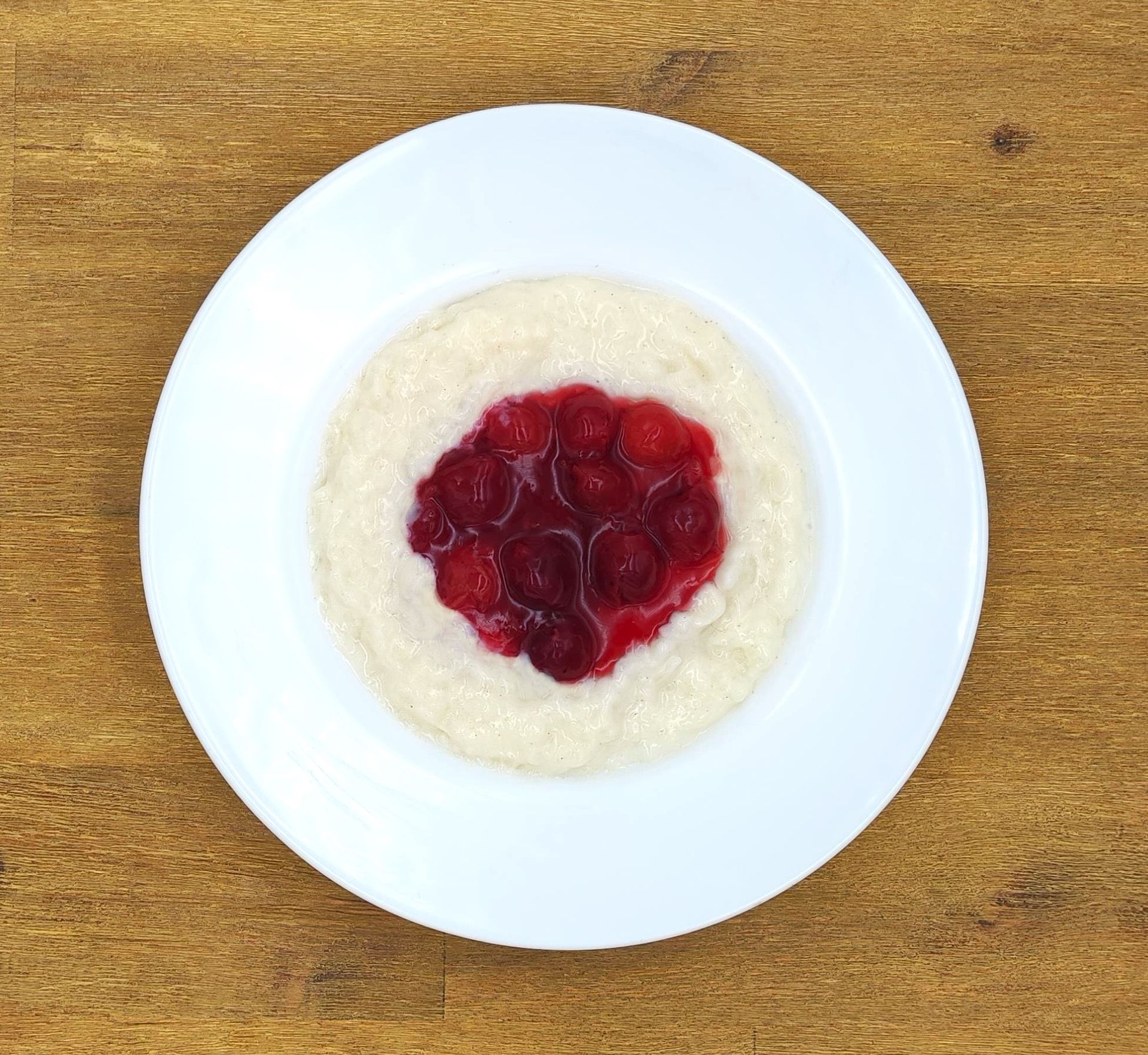 Weißer Haferbrei mit rotem Fruchtkompott in einer weißen Schüssel auf einer Holzoberfläche.