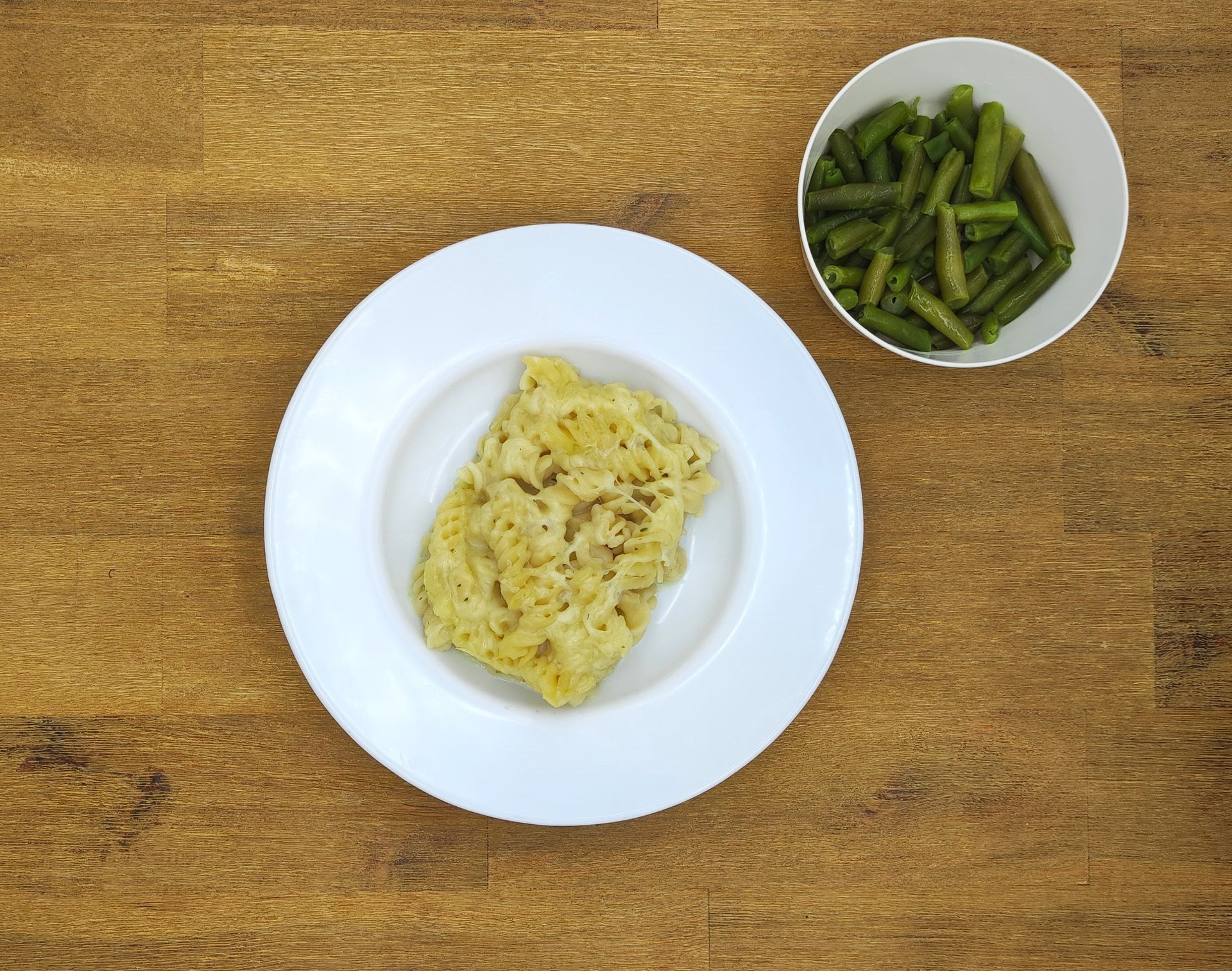 Ein Teller mit cremiger Speise und grünen Bohnen in einer Schüssel, auf einer Holzoberfläche angerichtet.
