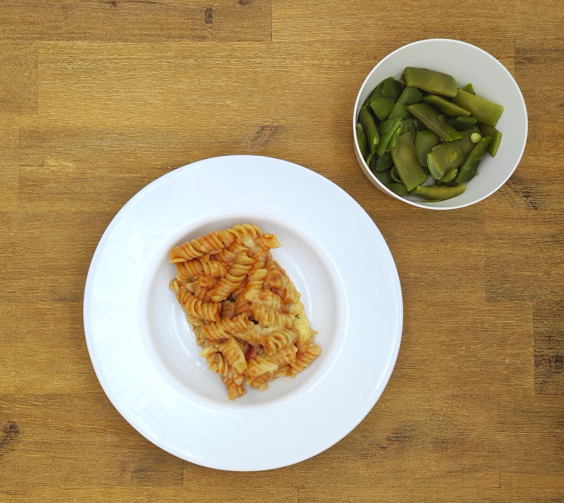 Pastagericht mit grünen Bohnen als Beilage auf einem Holztisch.