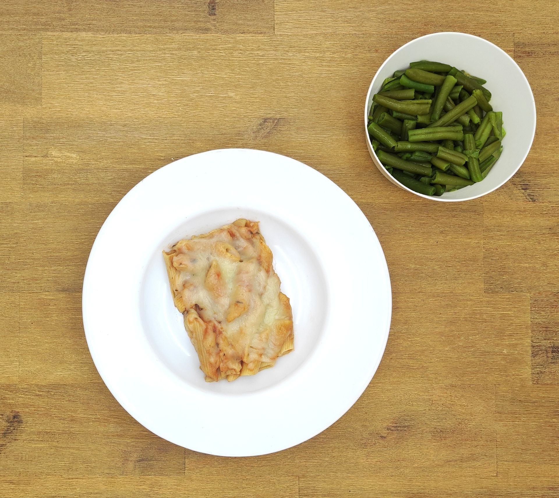 Teller mit paniertem Fleisch und Schüssel mit grünen Bohnen auf einer Holzoberfläche.