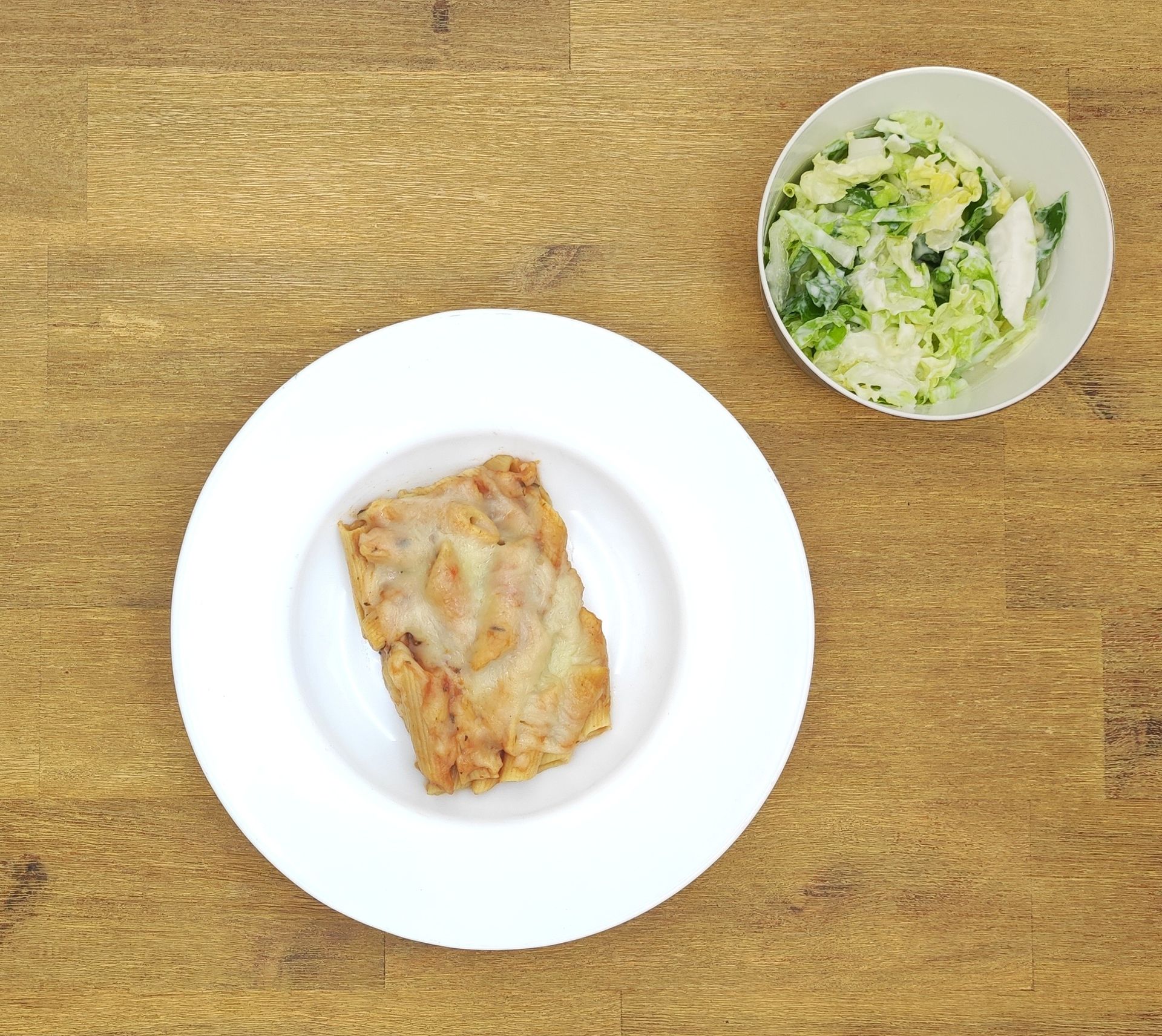 Weiße Schüssel mit Linsensuppe und Brot auf einer Holzoberfläche.