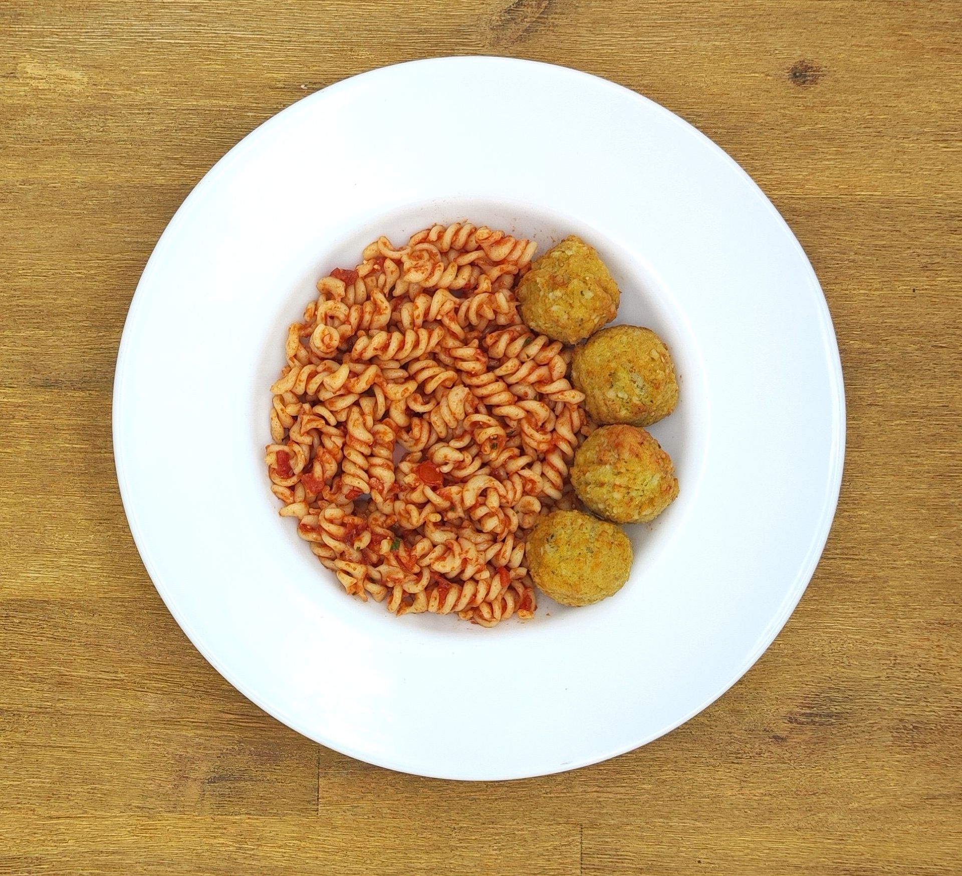 Pasta mit Tomatensoße und drei Fleischbällchen in einer weißen Schüssel auf einer Holzoberfläche.