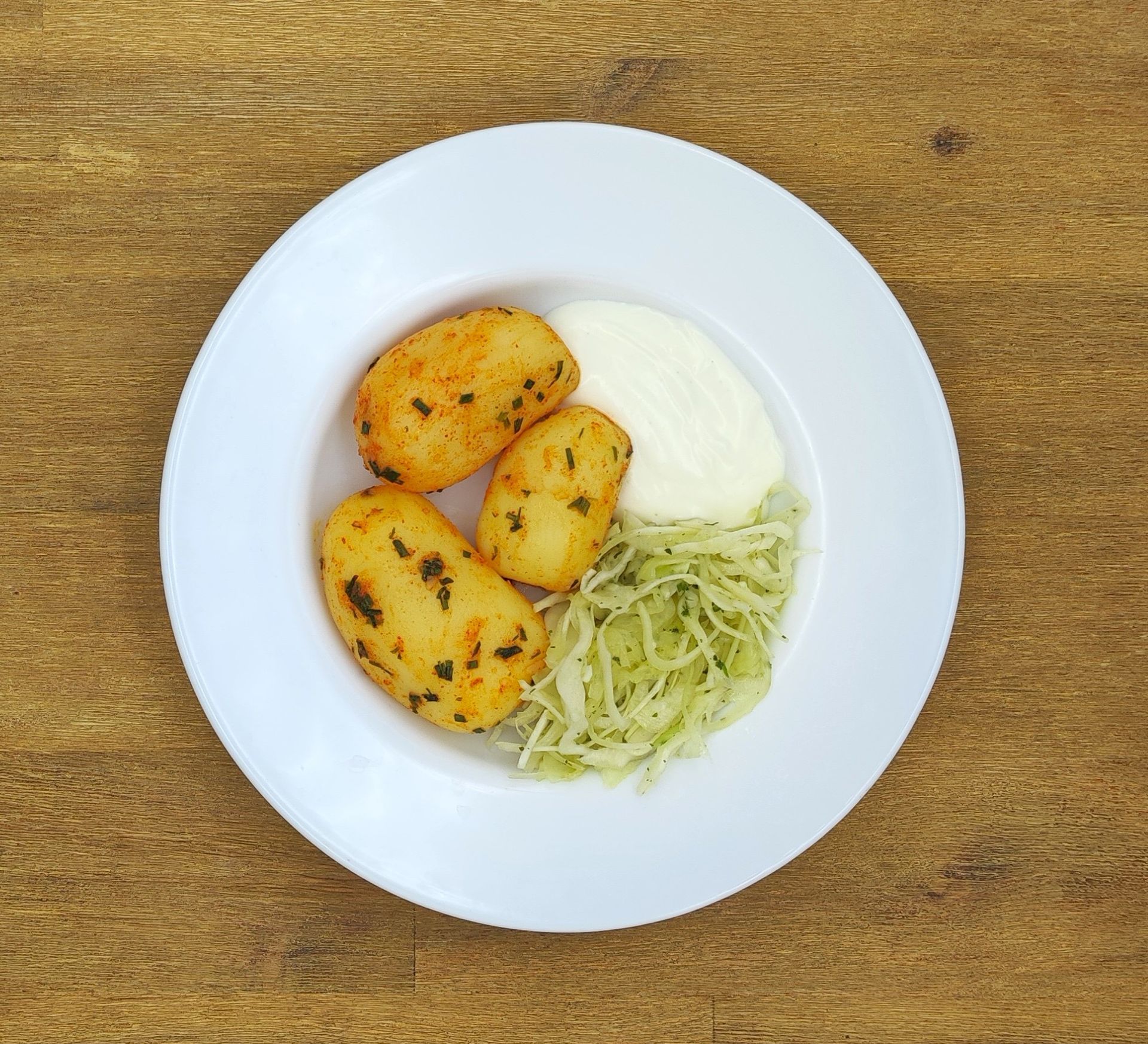 Gebratene Kartoffeln mit Krautsalat und weißer Soße auf einem weißen Teller.