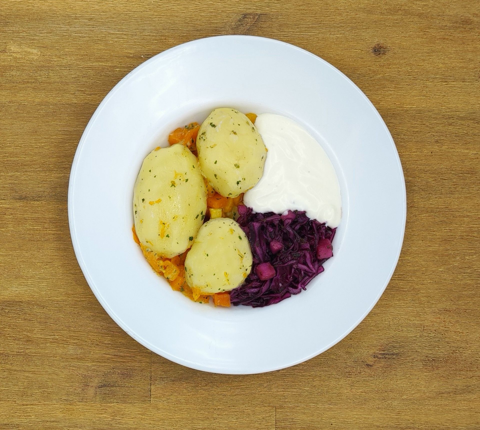 Ein Teller mit Essen: Kartoffeln, Rotkohl, Soße und Karotten auf einer Holzoberfläche.