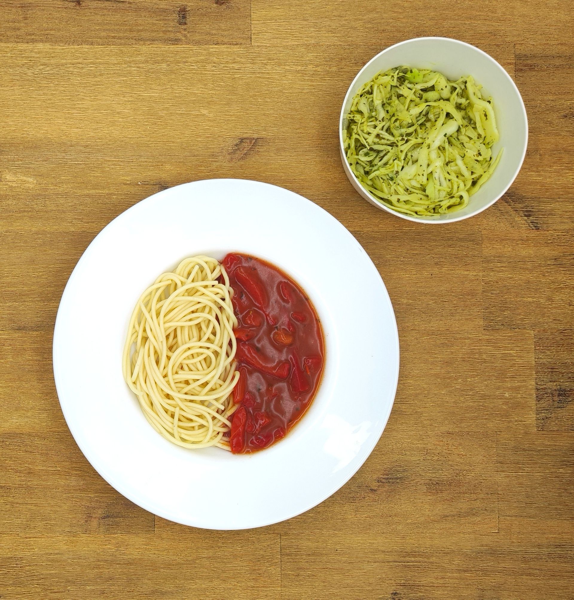 Spaghetti mit Tomatensoße und dazu Pesto-Pasta auf einem Holztisch.