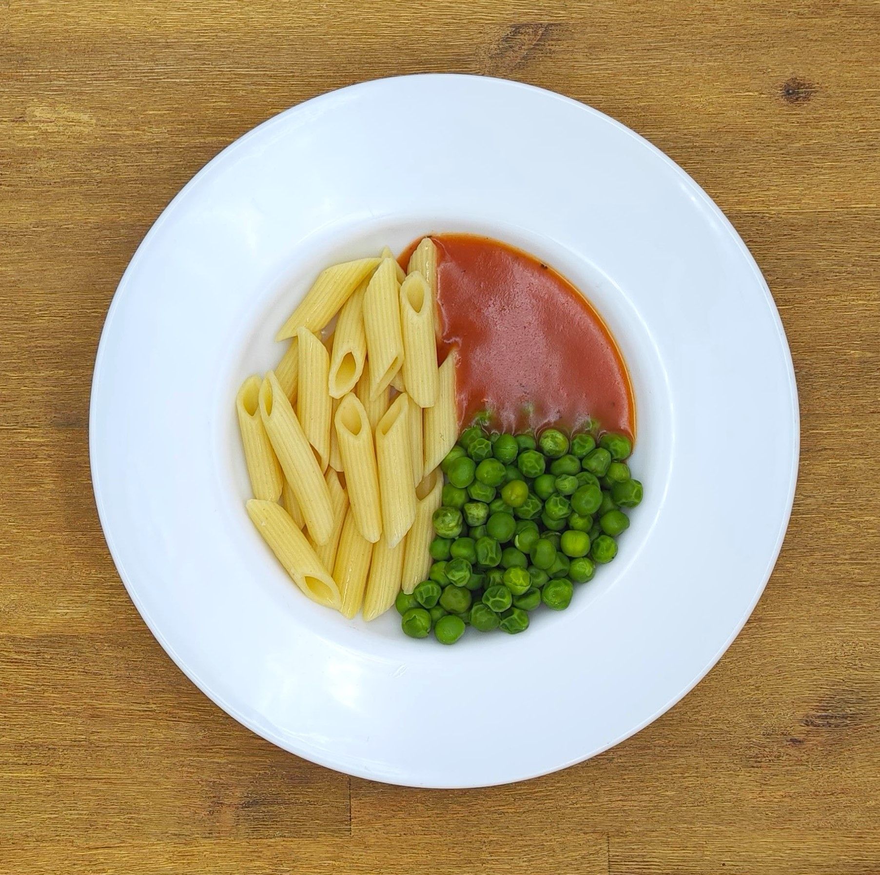 Weißer Teller mit Penne-Nudeln, Tomatensoße und Erbsen.