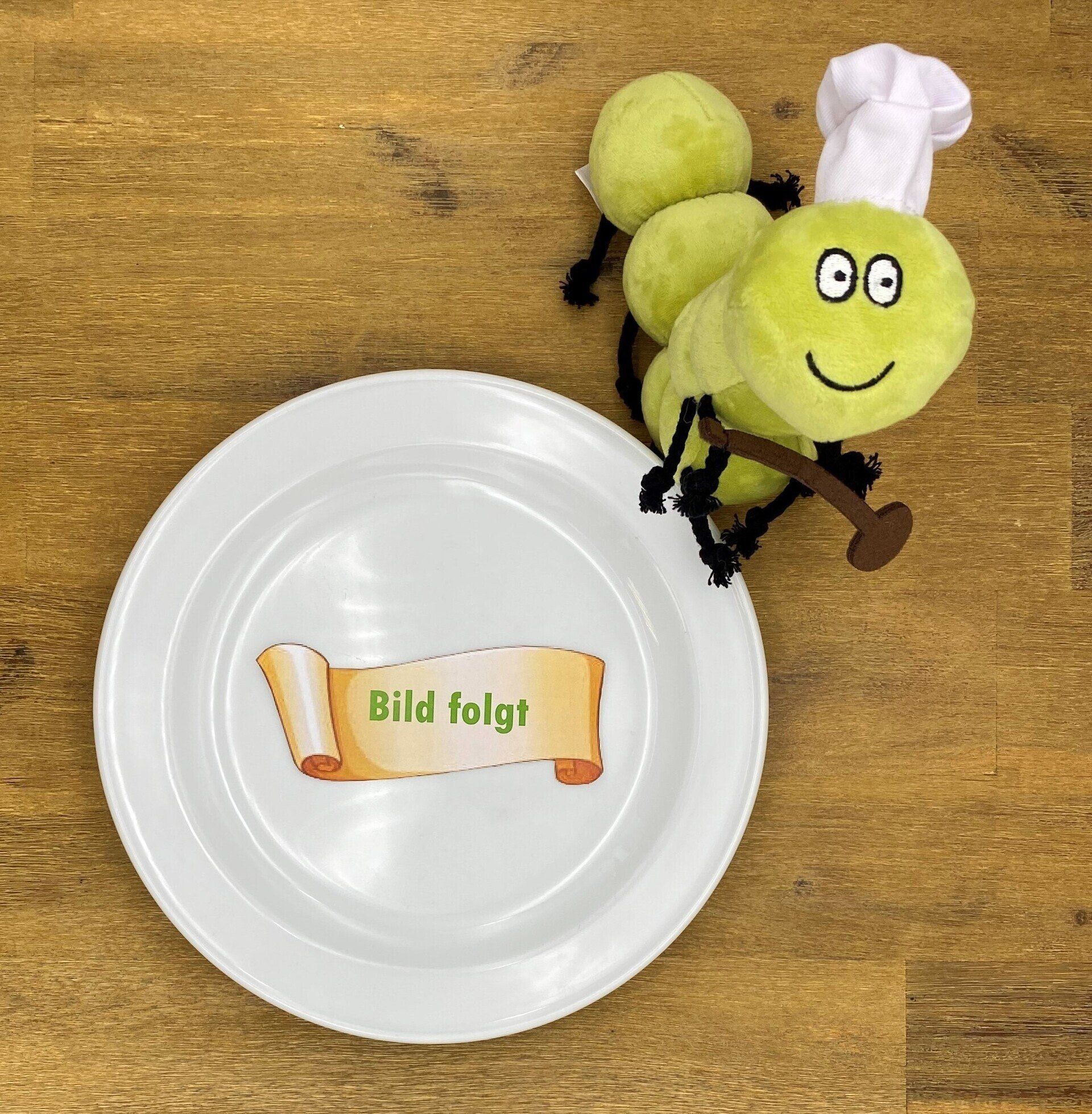 Ein grüner, ausgestopfter Raupenkoch mit einem Teller, auf dem „Bild folgt“ auf einer Holzoberfläche steht.