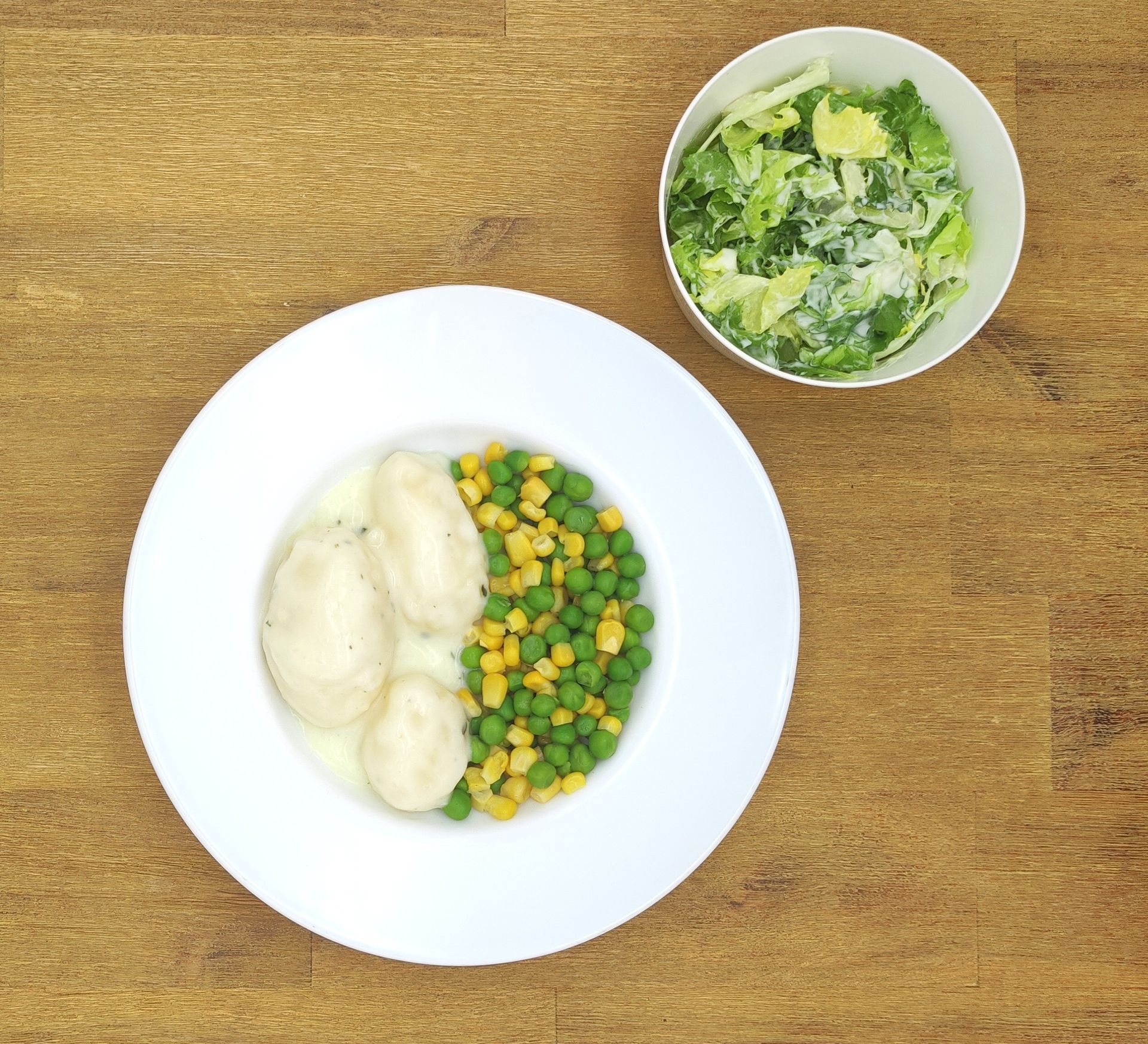 Teller mit Hühnerknödeln, Mais und Erbsen, Caesar Salad in einer Schüssel.