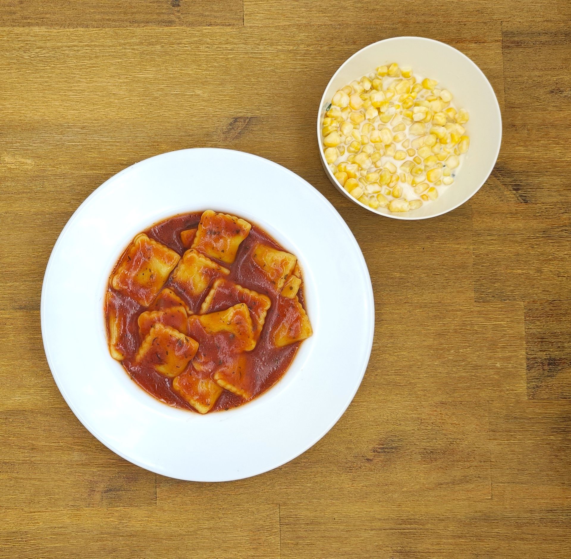 Nudeln in Tomatensoße und eine Schüssel Mais auf einem Holztisch.