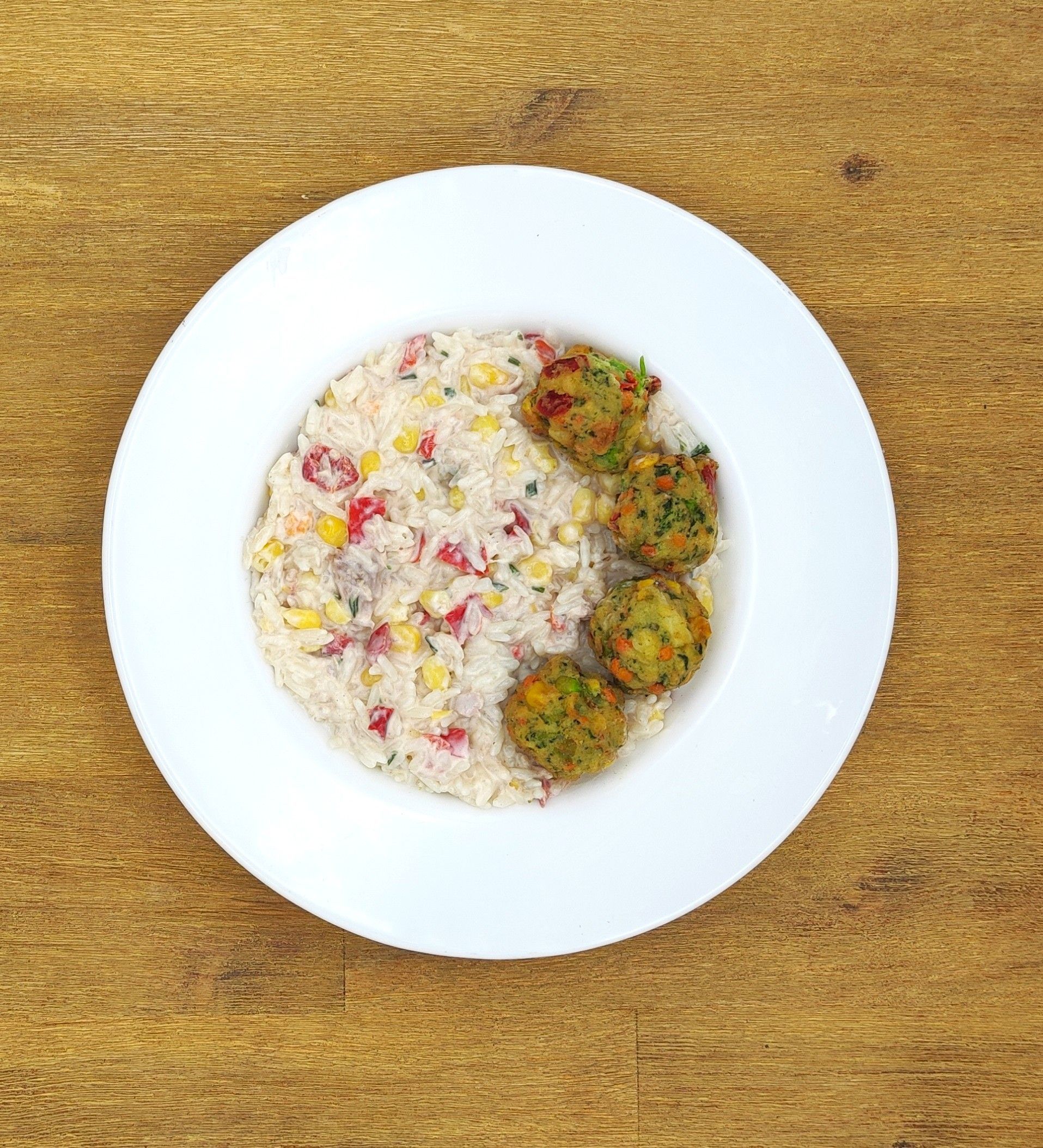 Weißer Teller mit Reis und Gemüsebällchen auf einem Holztisch.