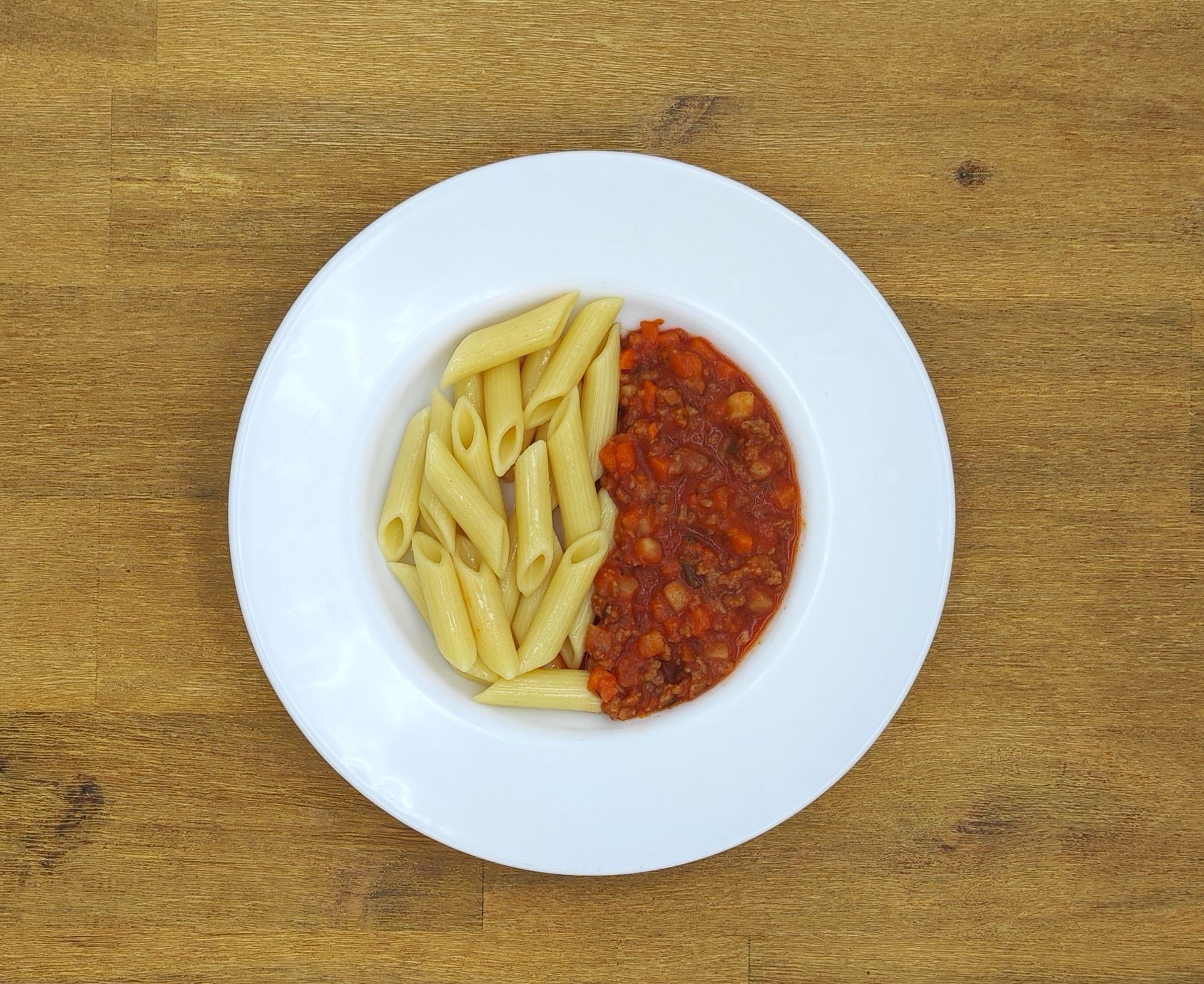 Penne-Nudeln mit roter Soße auf einem weißen Teller, der auf einem Holztisch steht.