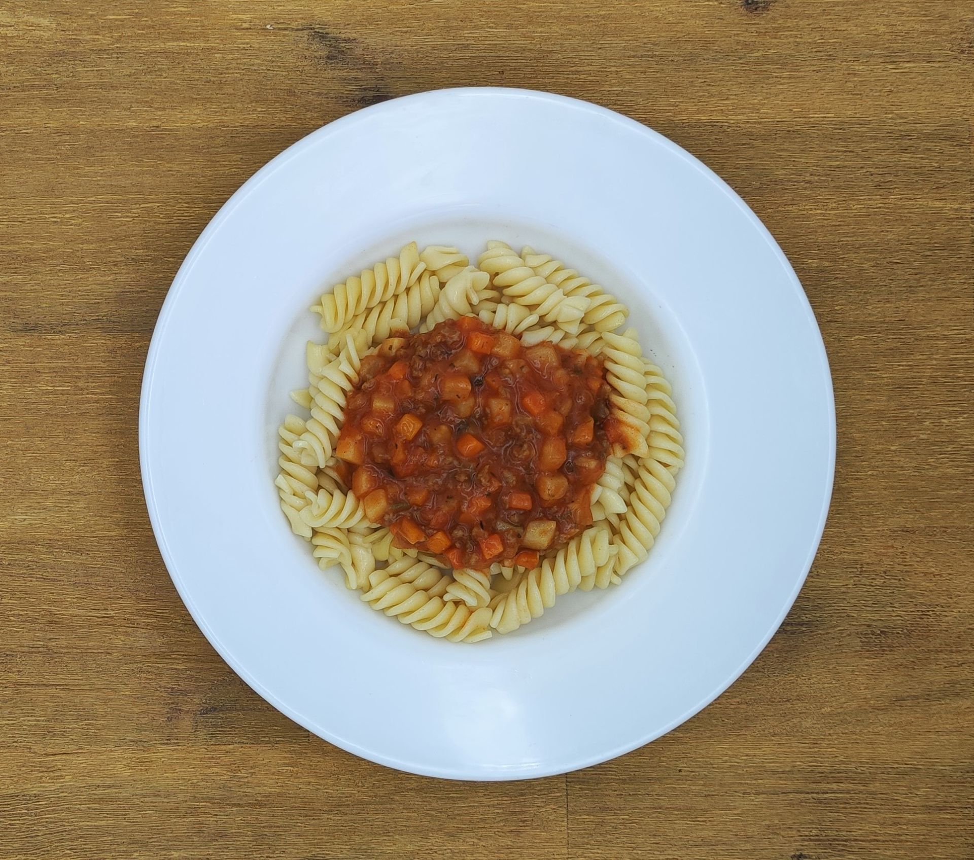 Ein Teller Pasta mit roter Soße auf einem Holztisch.