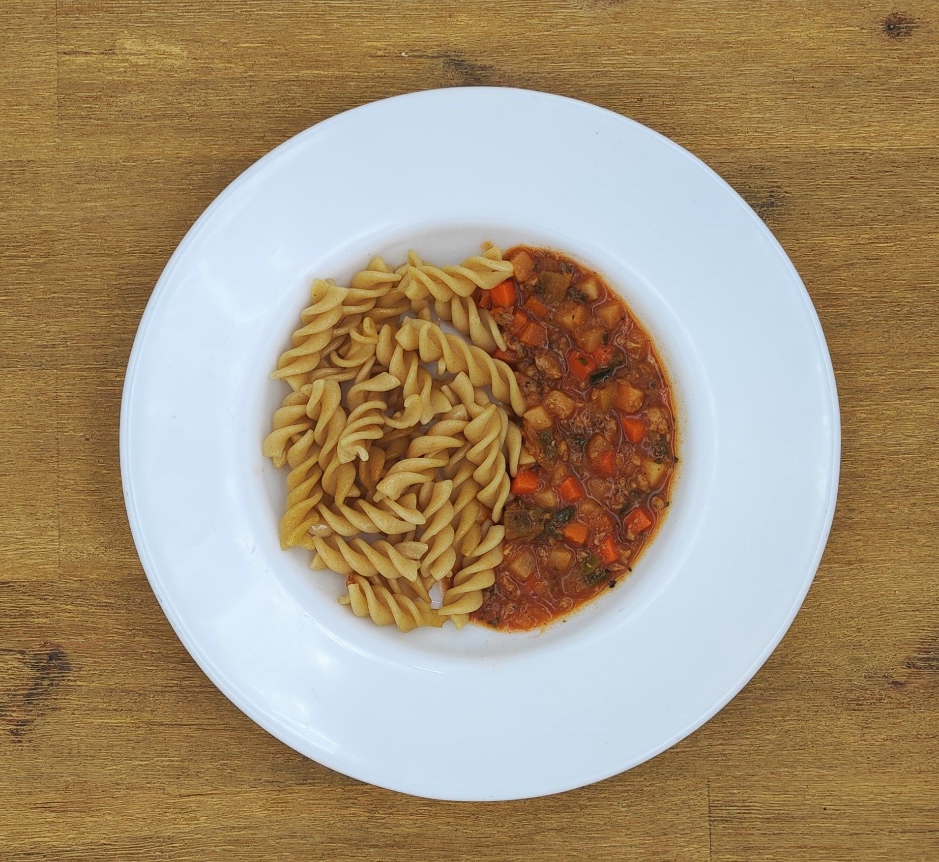 Weißer Teller mit braunen Spiralnudeln und rotbrauner Gemüsesauce.