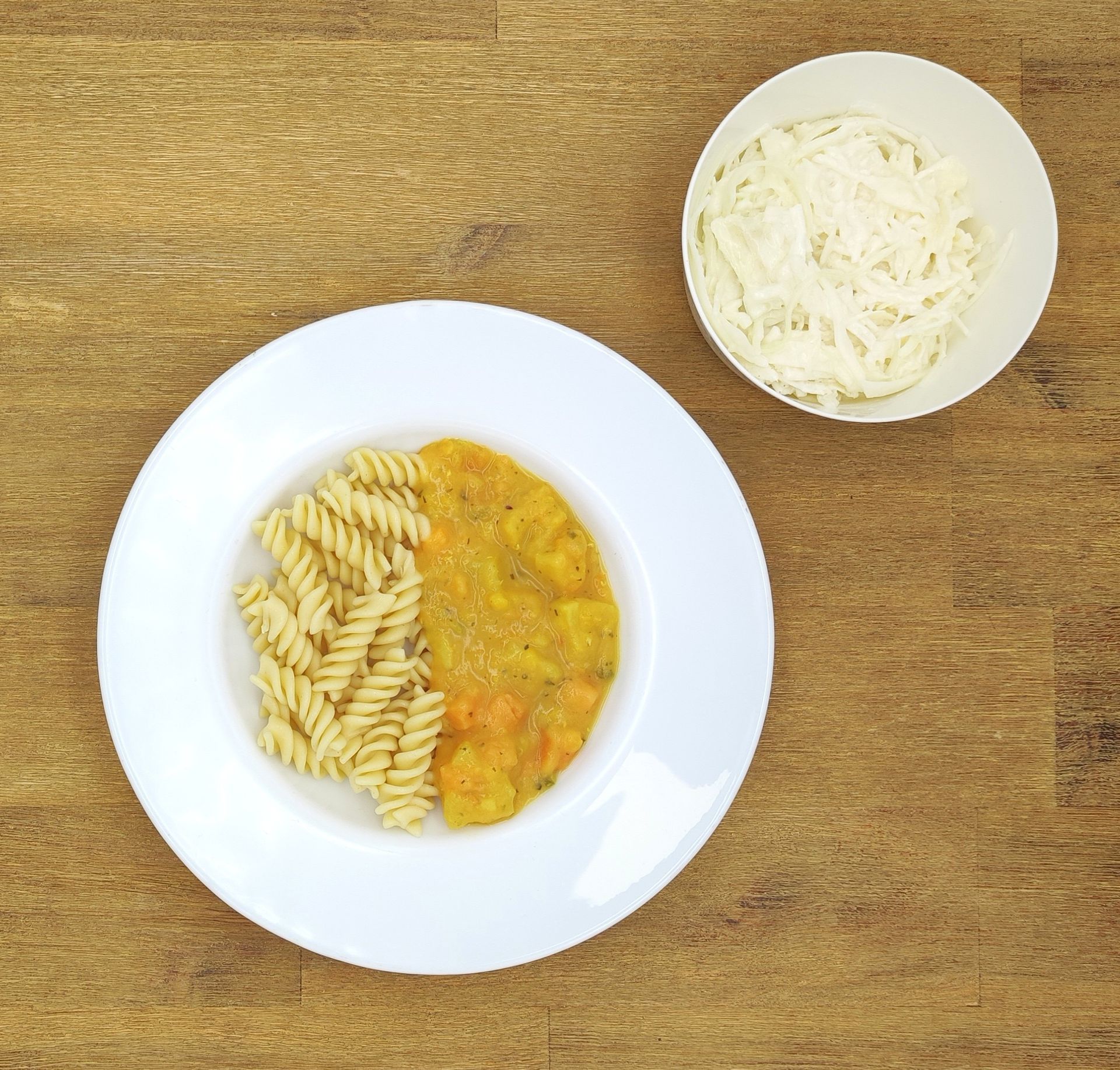 Weiße Schüssel mit Linsensuppe und Brot auf einer Holzoberfläche.