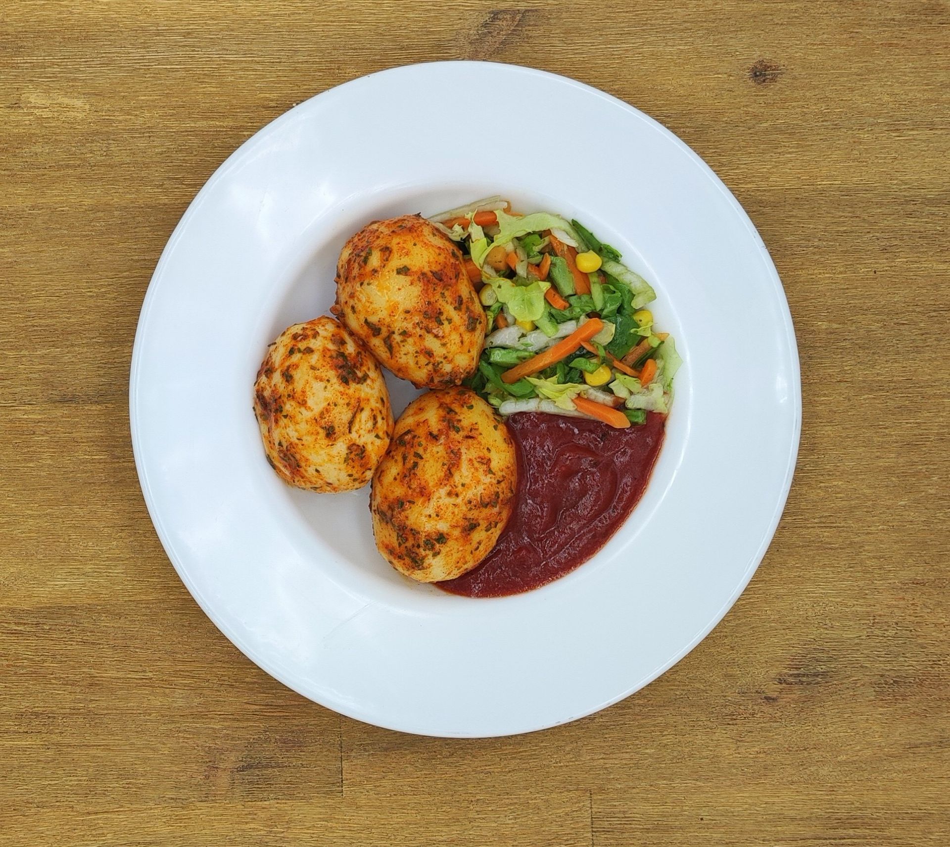 Weißer Teller mit drei gewürzten Kartoffelkroketten, Salat und roter Soße.