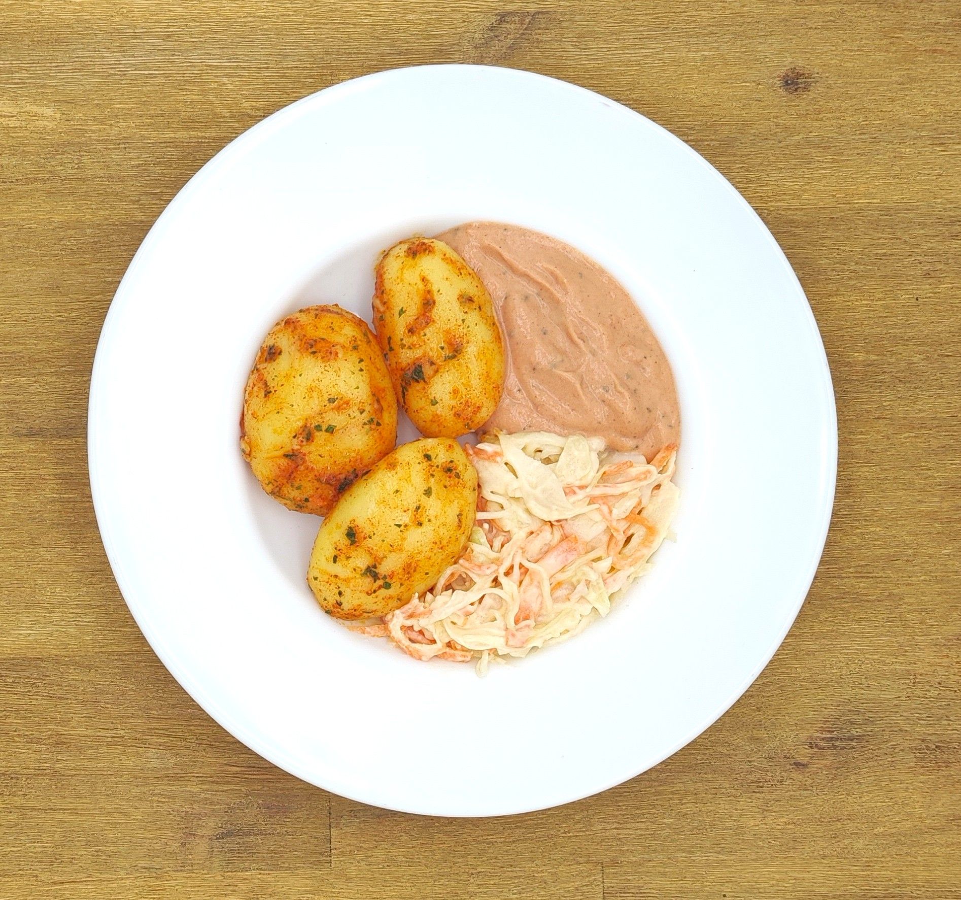 Weißer Teller mit gewürzten Kartoffeln, Bohnenpüree und Krautsalat.