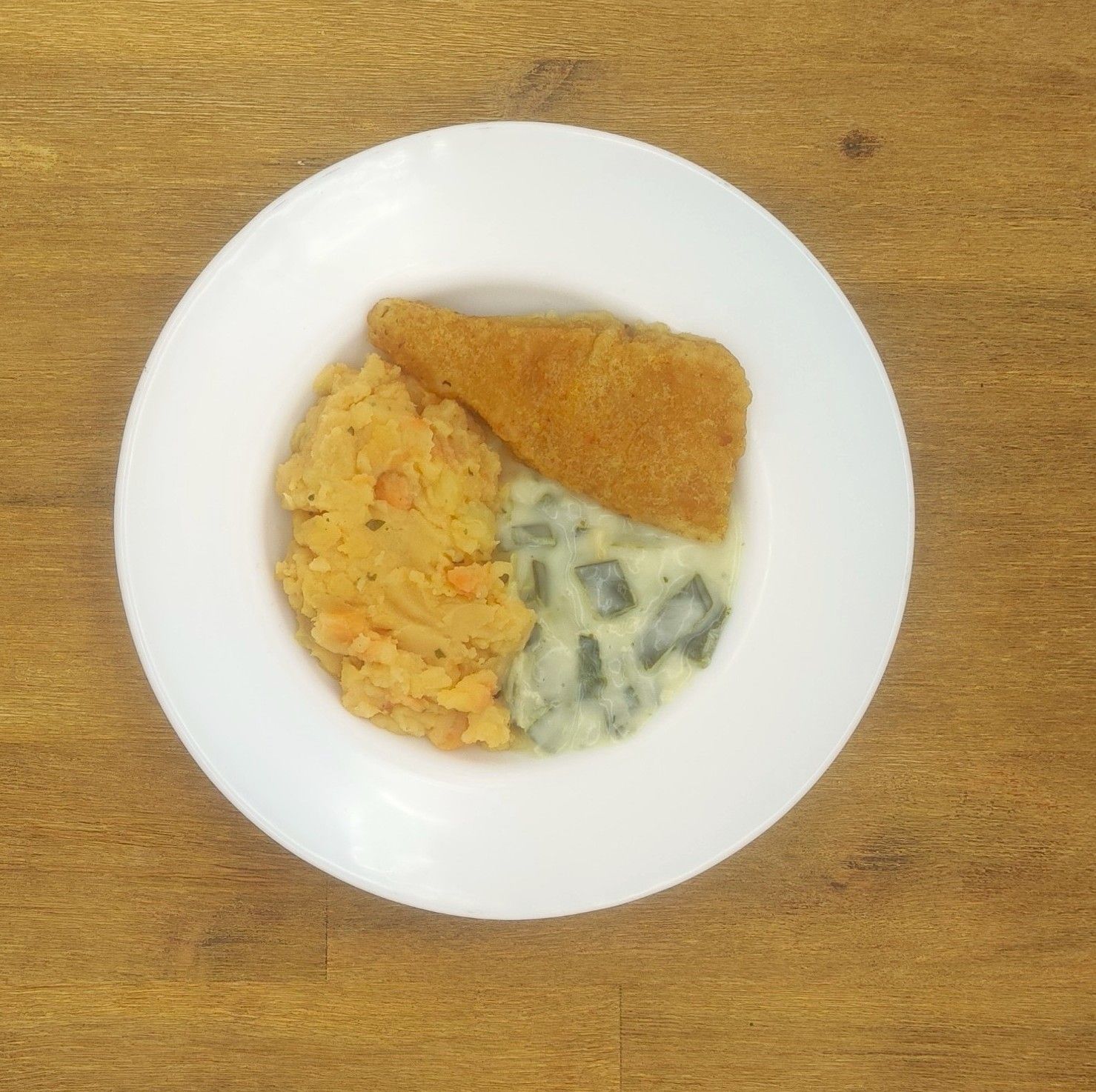 Tellergericht: paniertes Fischfilet, püriertes Gemüse und Rahmgemüse.