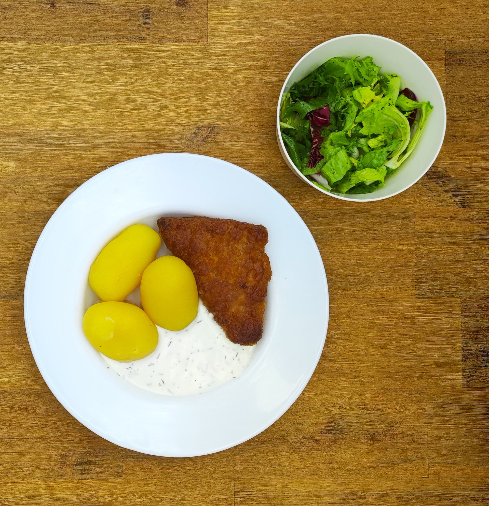 Tellergericht: paniertes Fleisch, Salzkartoffeln, Soße und ein Beilagensalat.