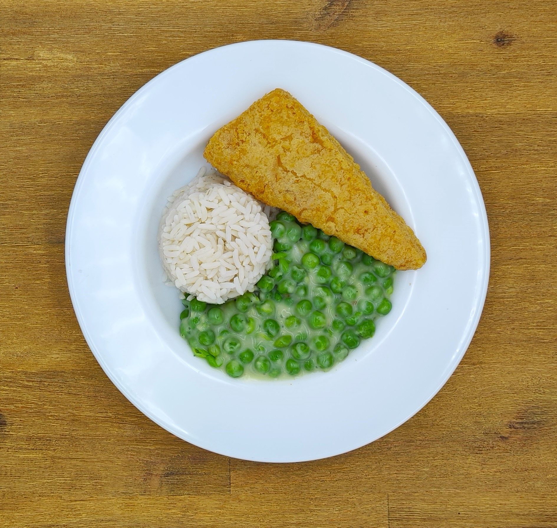 Teller mit paniertem Fisch, Reis und Erbsen in Soße.