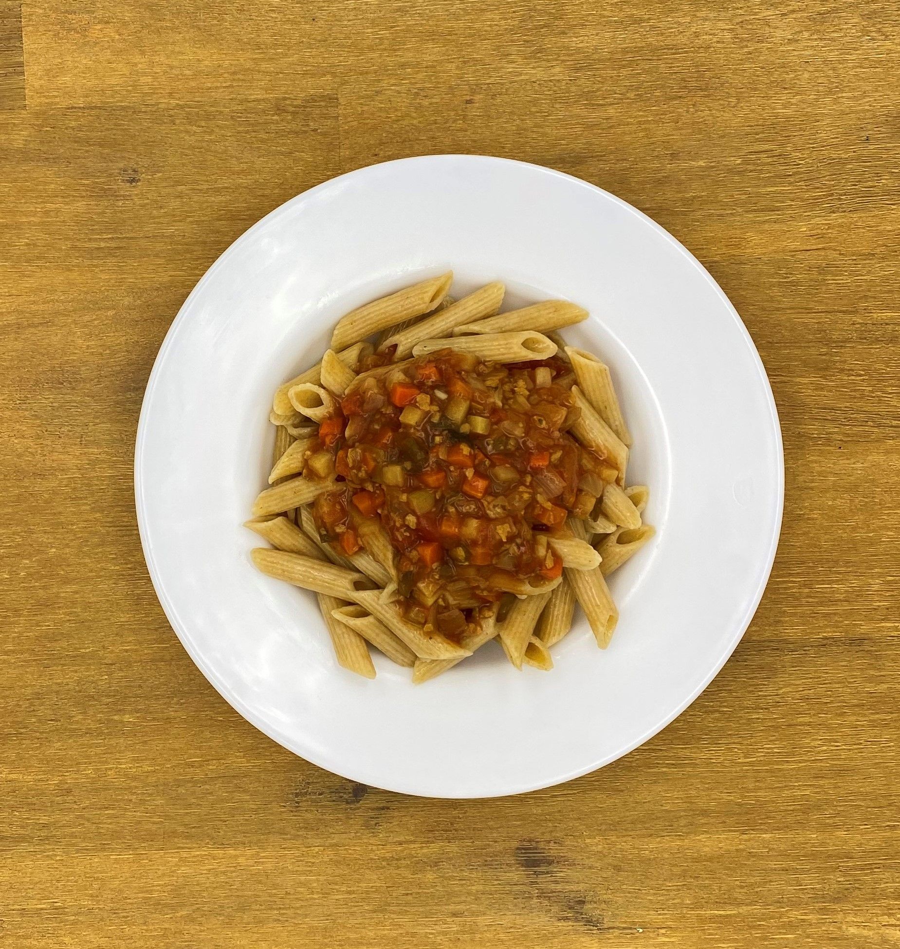 Penne-Nudeln mit roter Soße in einer weißen Schüssel auf einem Holztisch.