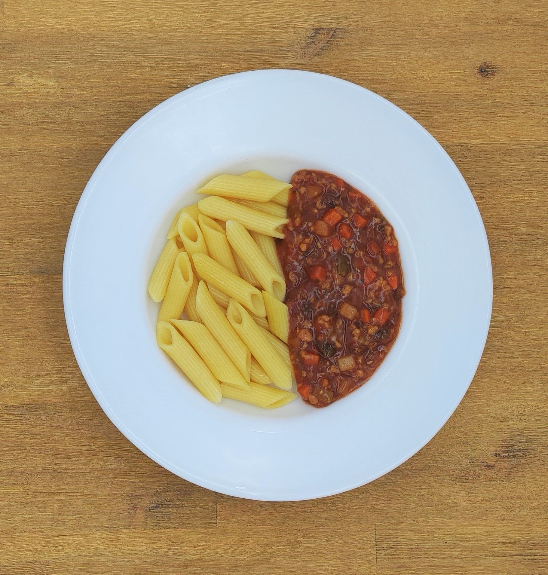 Pasta mit Fleischsoße auf Tomatenbasis auf einem weißen Teller, der auf einer Holzoberfläche steht.