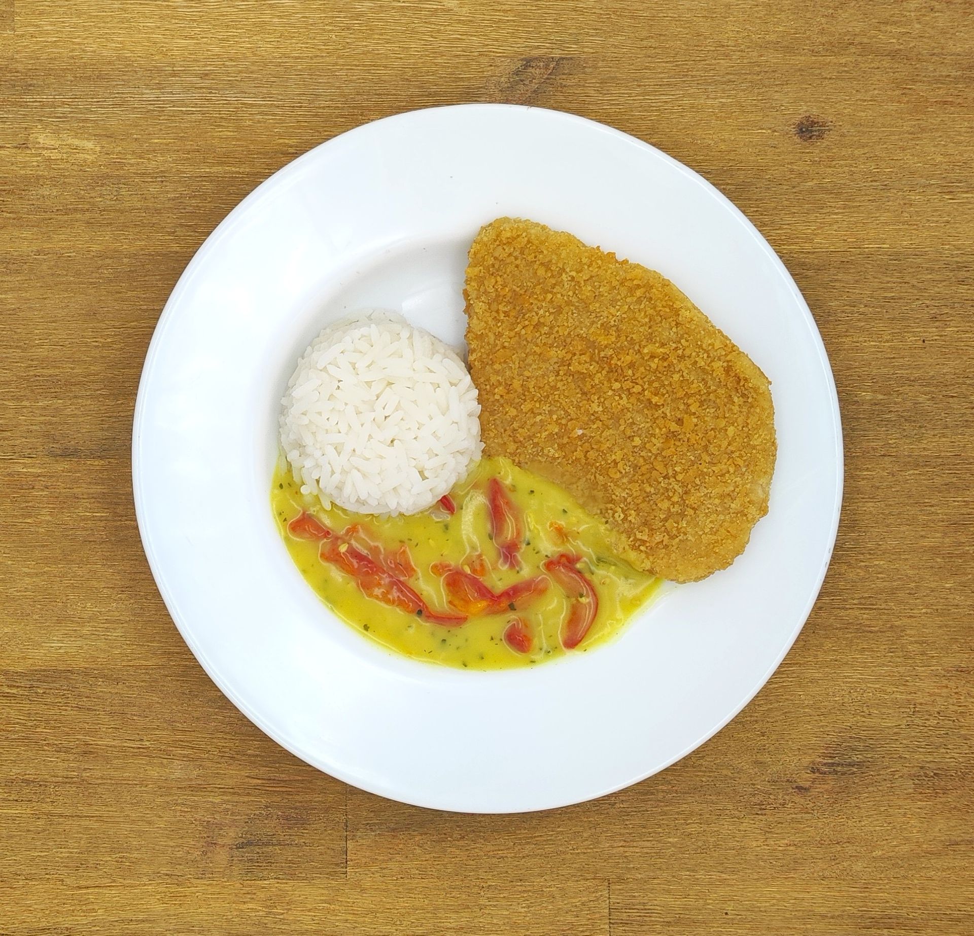 Teller mit paniertem Hähnchen, Reis und Currysauce.