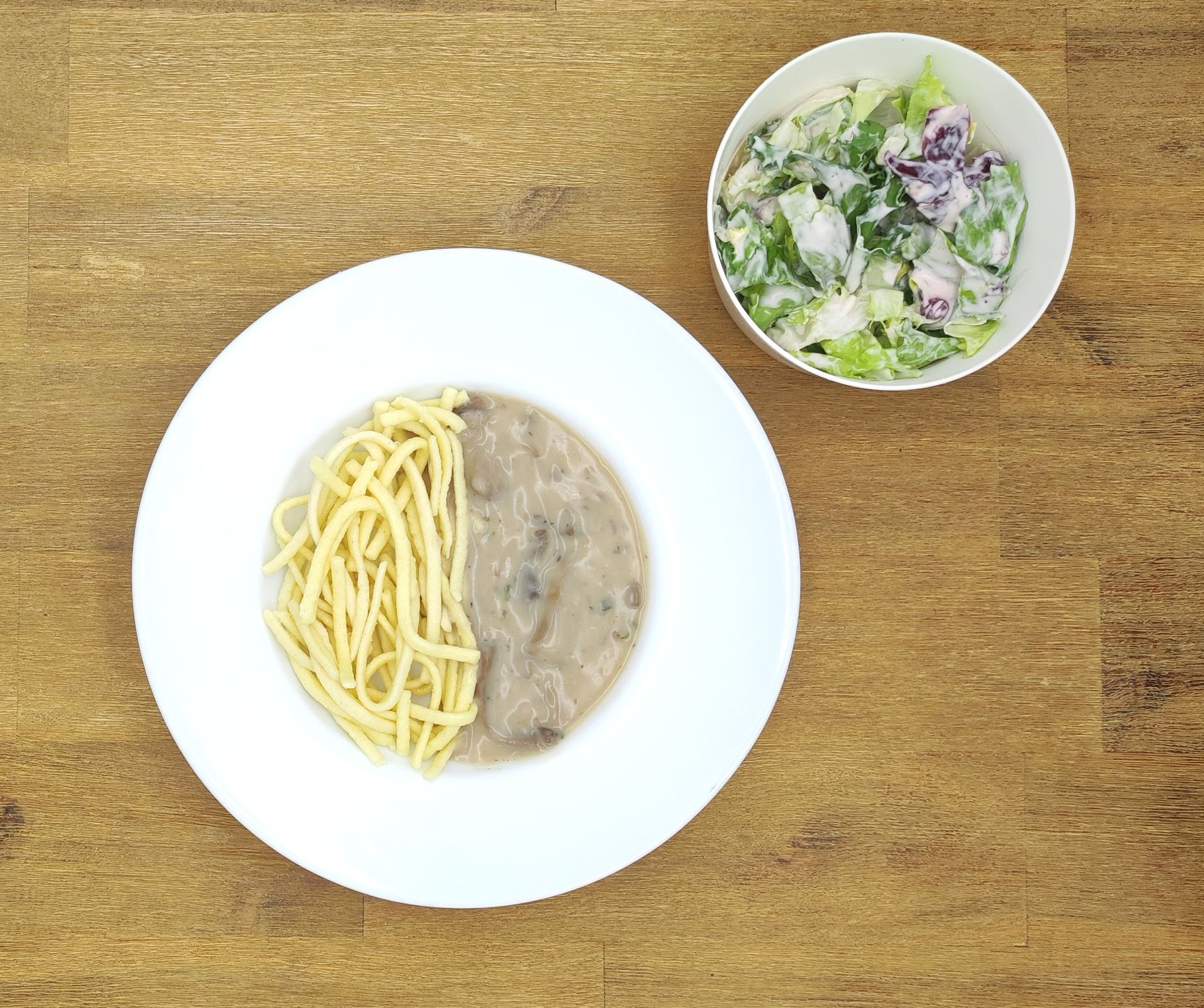 Eine grüne Plüschraupe mit Kochmütze hält einen Löffel über einem Teller mit der grünen Aufschrift „Bild folgt“.