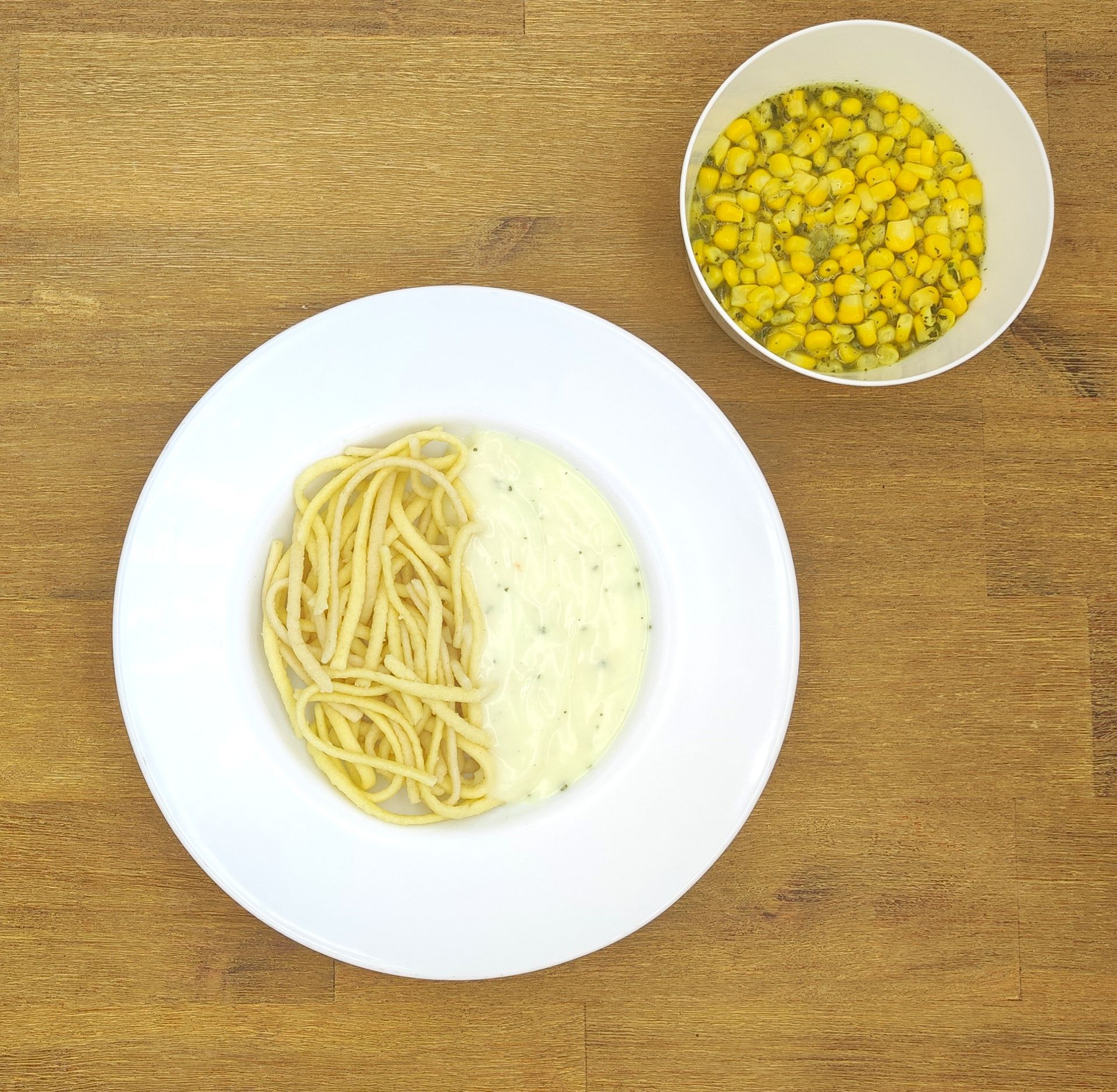 Pastagericht mit Spaghetti, Käse und Mais als Beilage auf einem Holztisch.