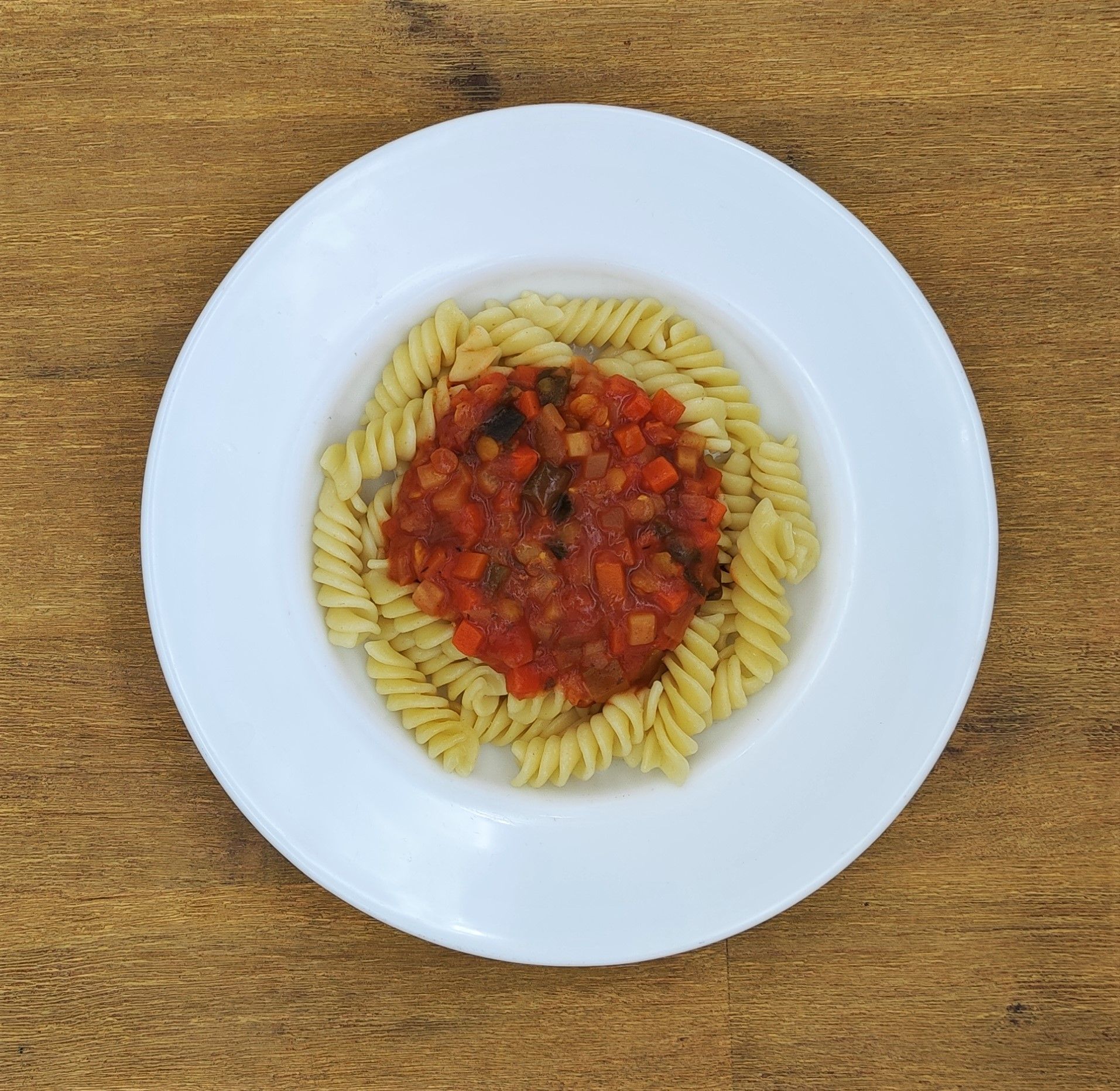 Pasta mit roter Soße auf einem weißen Teller, der auf einem Holztisch steht.