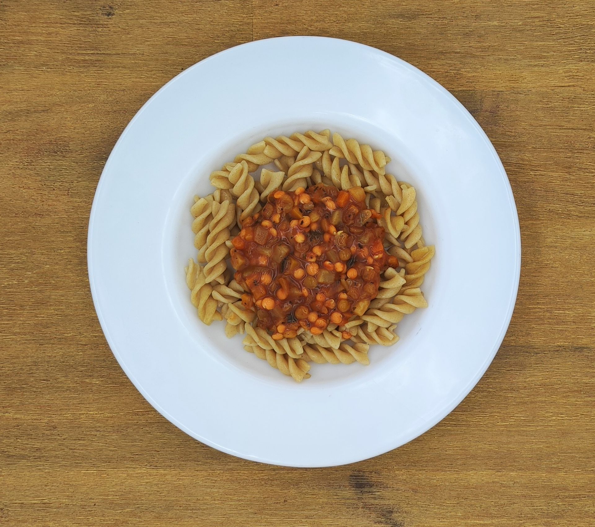 Pastagericht: Spiralnudeln mit einer Sauce auf Linsenbasis, mittig auf einem weißen Teller auf einem Holztisch angerichtet.