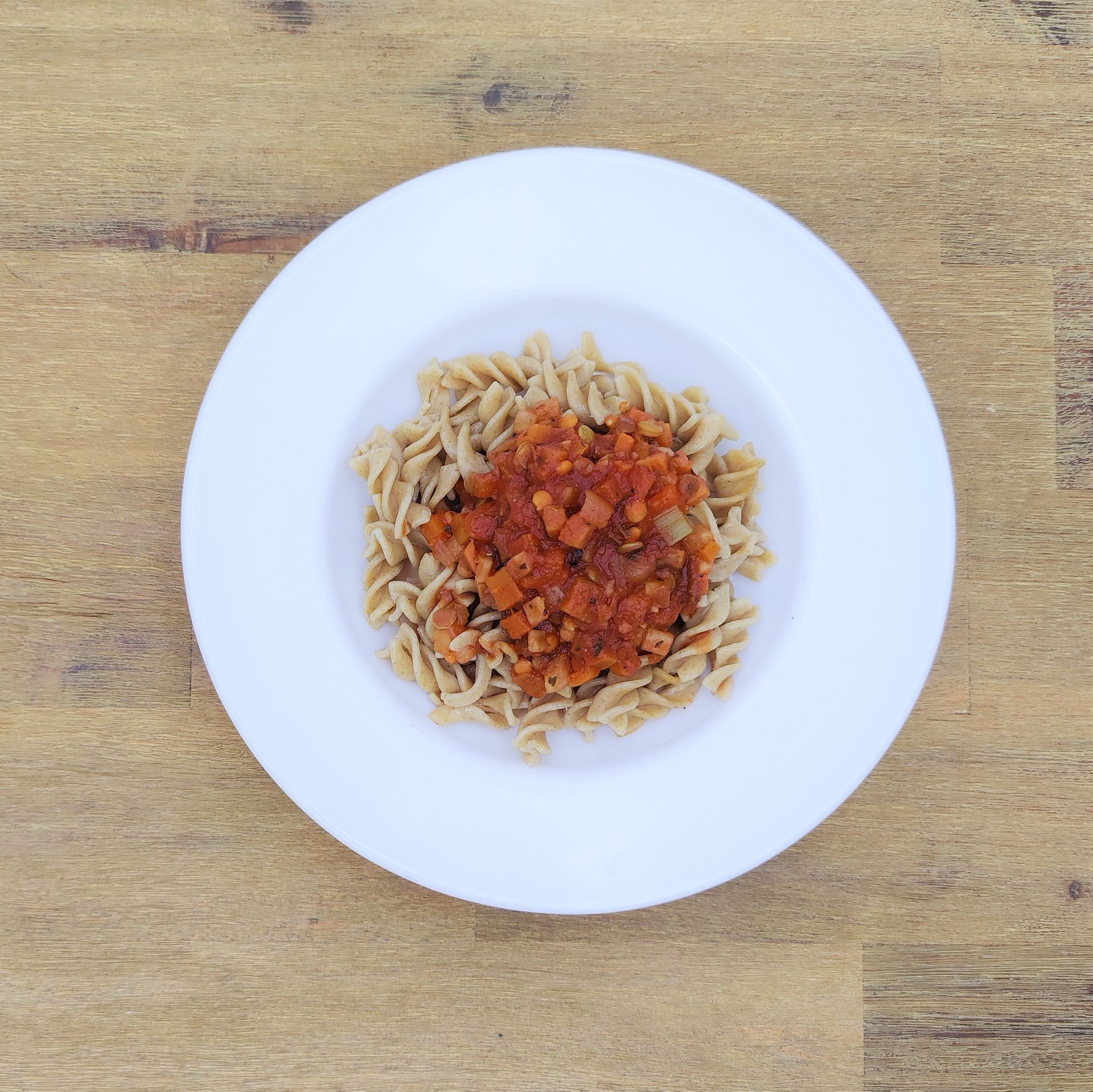 Ein Teller Pasta mit Tomatensoße auf einer Holzoberfläche.