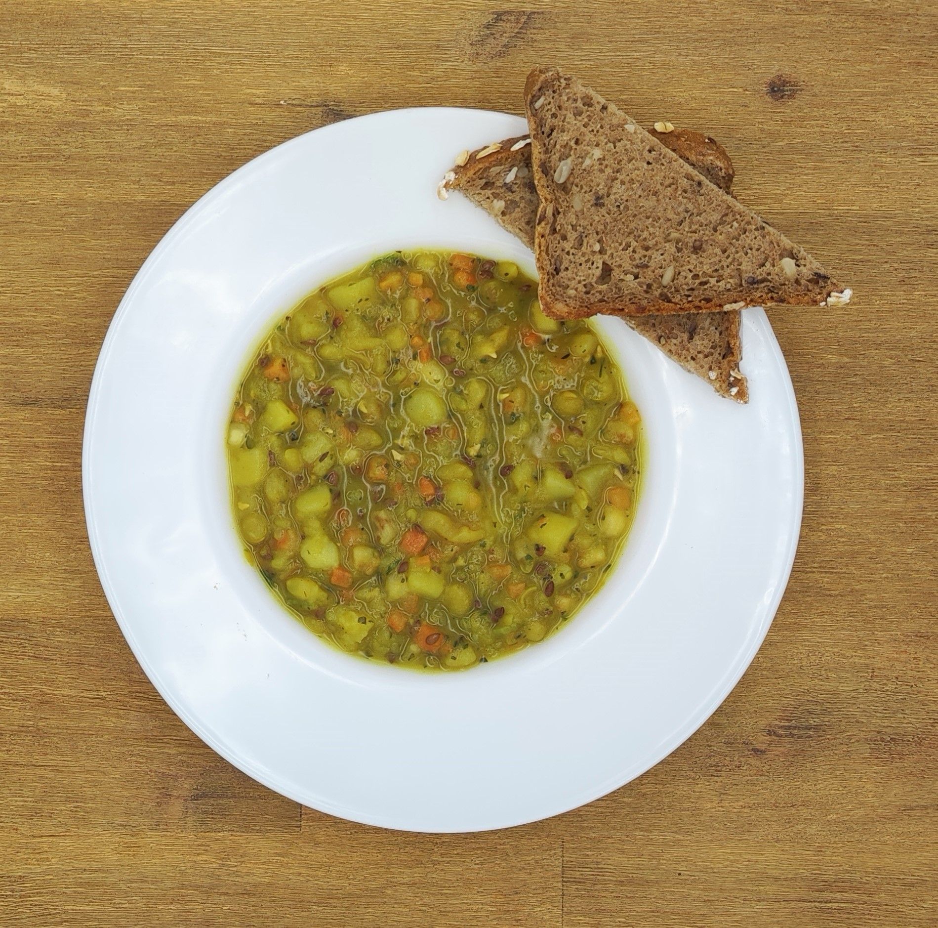 Suppe in einer weißen Schüssel mit Roggenbrot auf einem Holztisch.