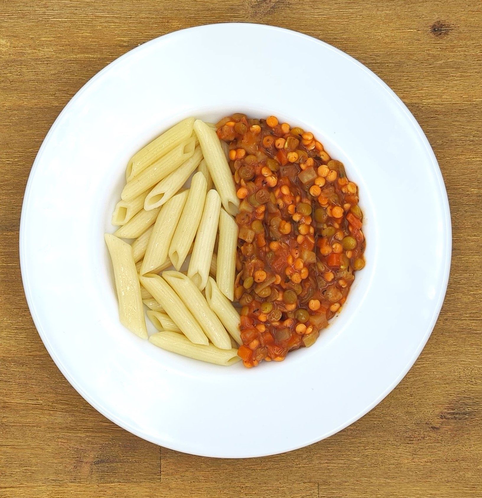 Weißer Teller mit Penne-Nudeln und Linseneintopf.
