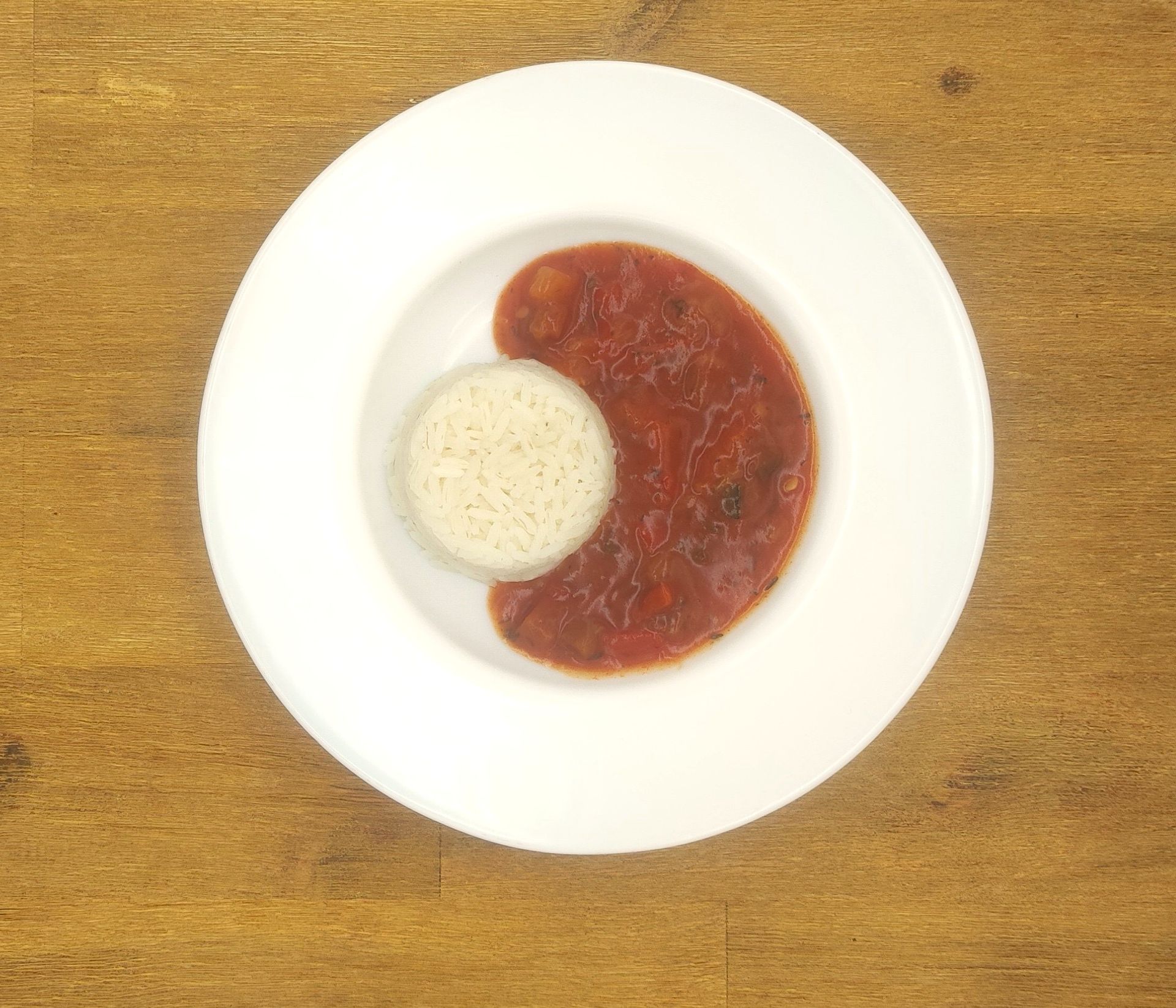 Ein weißer Teller mit Reis und einer großen Portion Tomatensoße, auf einer Holzoberfläche angerichtet.
