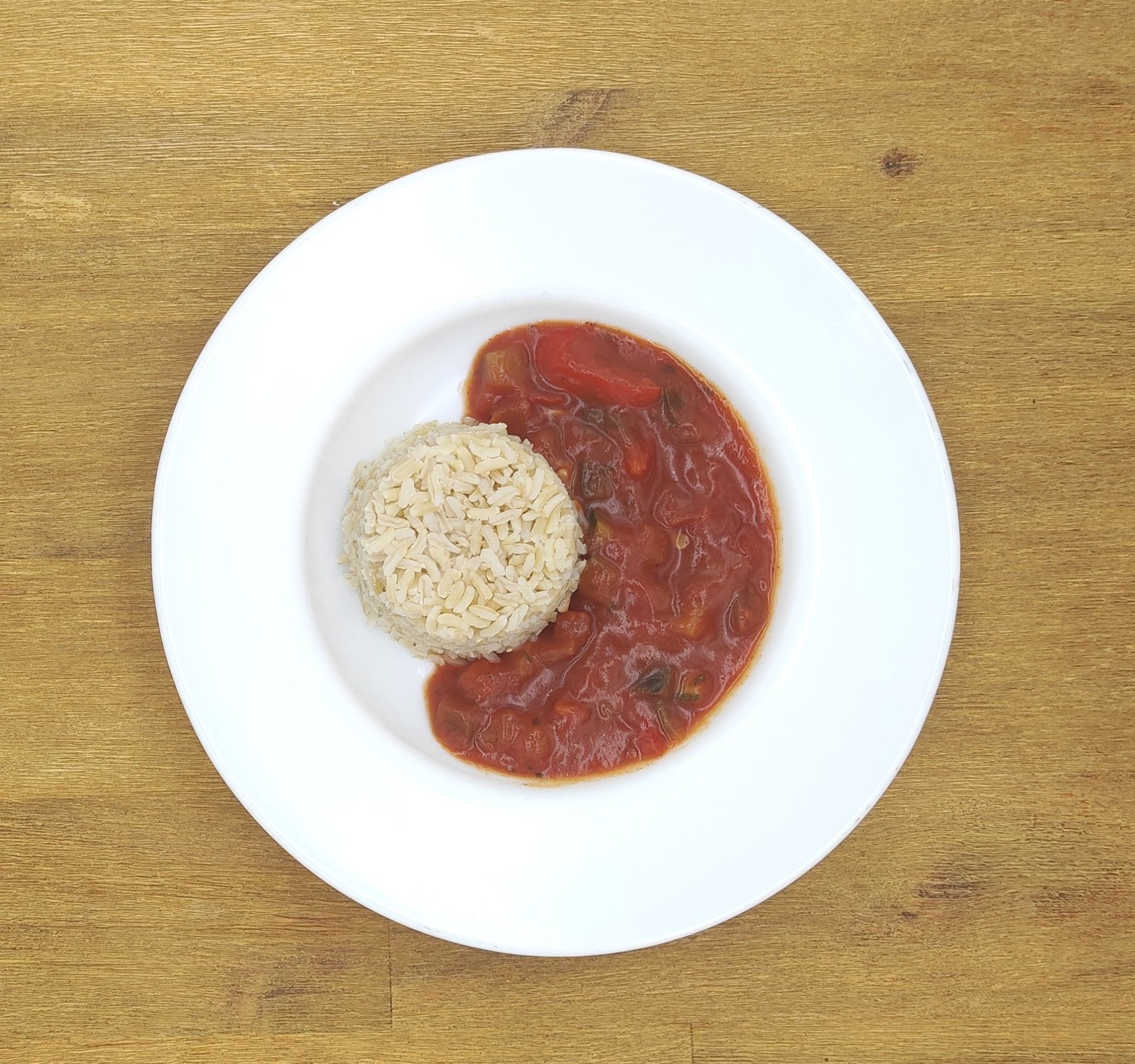 Ein Teller Reis neben geschmorten Tomaten auf einer Holzoberfläche.