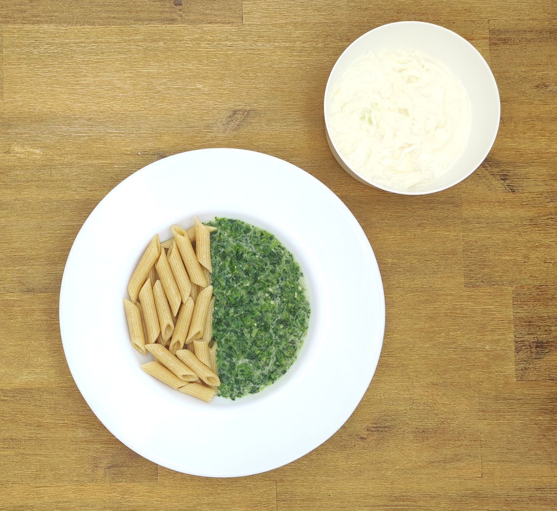 Weißer Teller mit Farfalle-Nudeln und Orangensauce, bestreut mit geriebenem Käse.