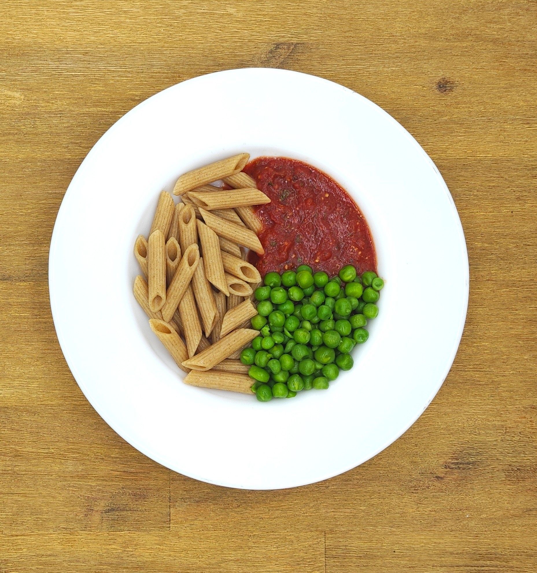 Weißer Teller mit Vollkorn-Penne-Nudeln, Tomatensoße und Erbsen.