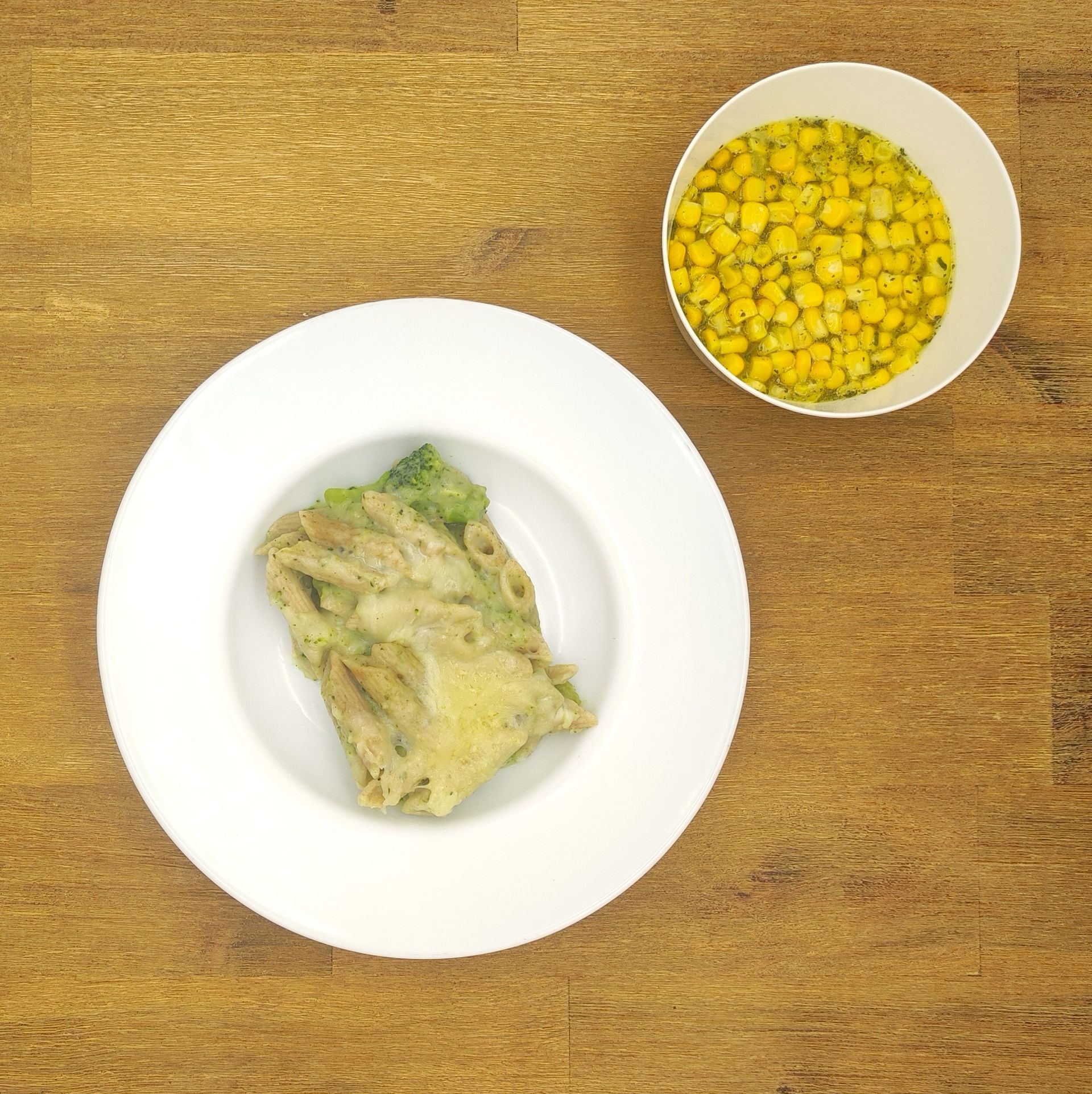 Pastagericht mit Brokkoli, serviert mit einer Schüssel Mais auf einem Holzbrett.
