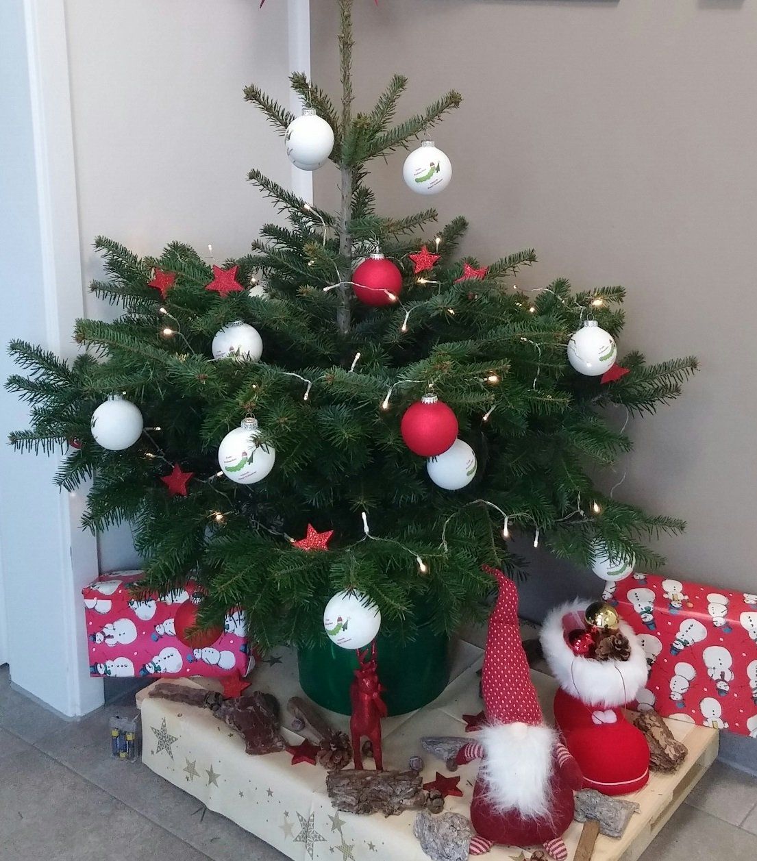 Kleiner, geschmückter Weihnachtsbaum mit Christbaumkugeln, Lichterketten und verpackten Geschenken.
