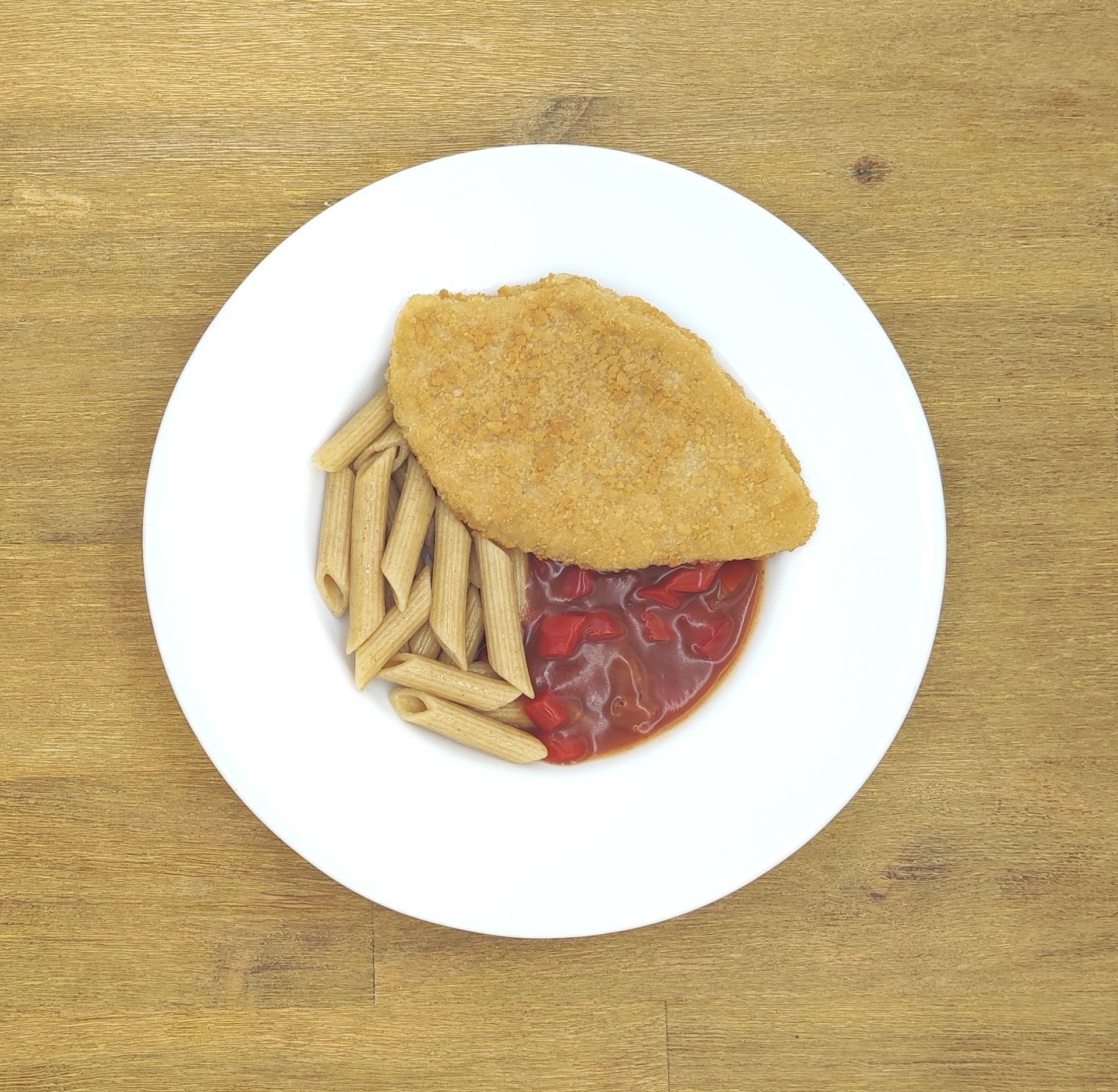 Ein Teller mit paniertem Hähnchen, Nudeln und Tomatensoße auf einem Holztisch.