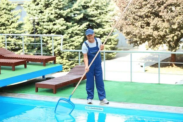 Worker cleaning an outdoor pool with a leaf net.