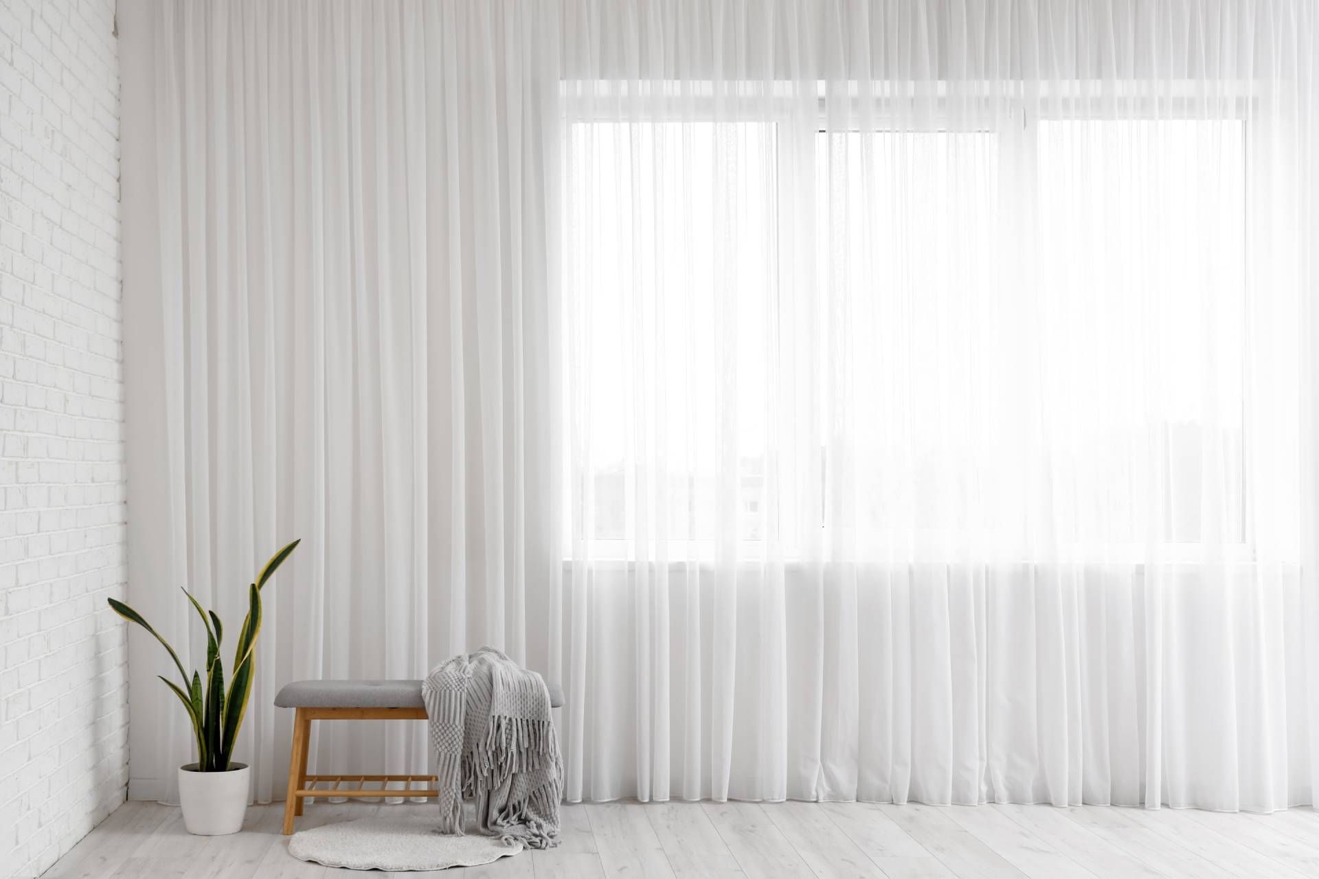 A light curtain near a plant, bench, blanket, and rug at Awnings, Blinds, and Shutters By Albert’s S