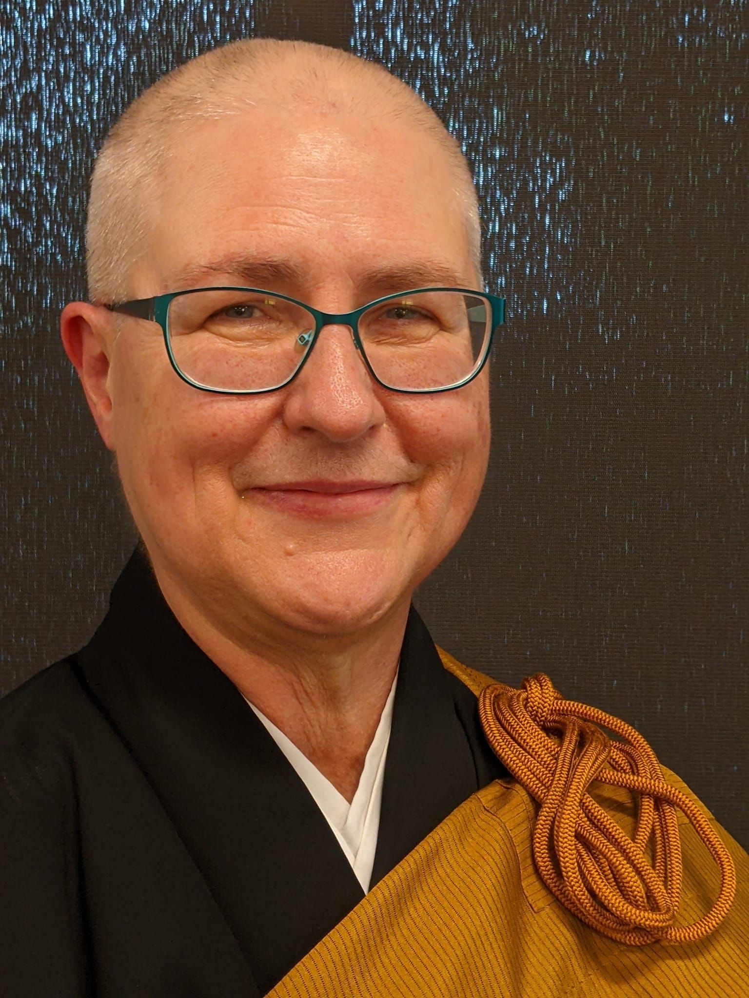 A picture of Janine Larsen dressed in Zen Priest robes and with shaved head.