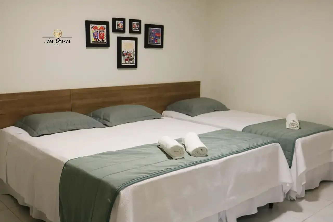 Um quarto de hotel com três camas e fotos na parede.hotel-asa-branca