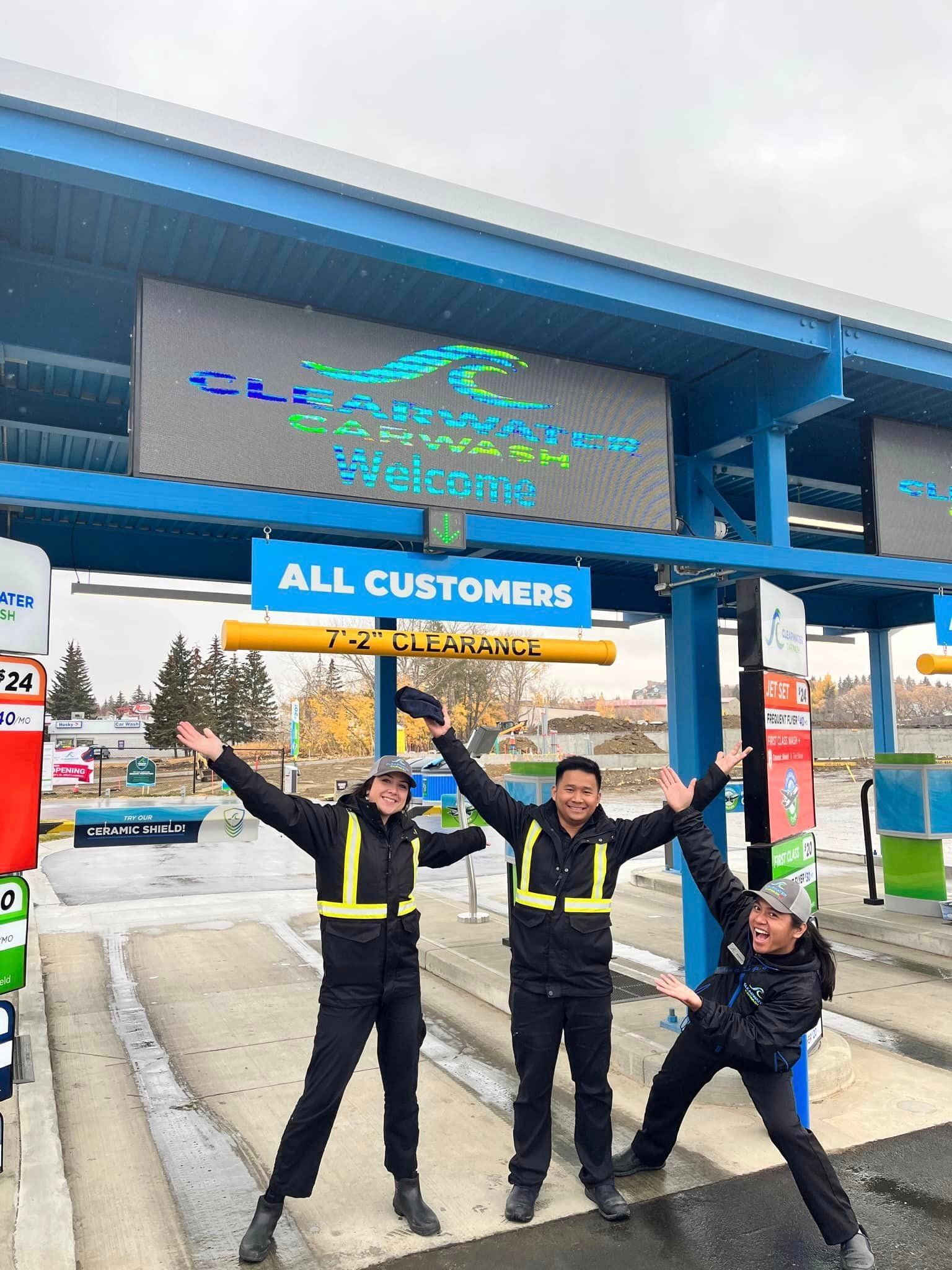 three crew members stand under LED sign that says clearwater carwash welcome