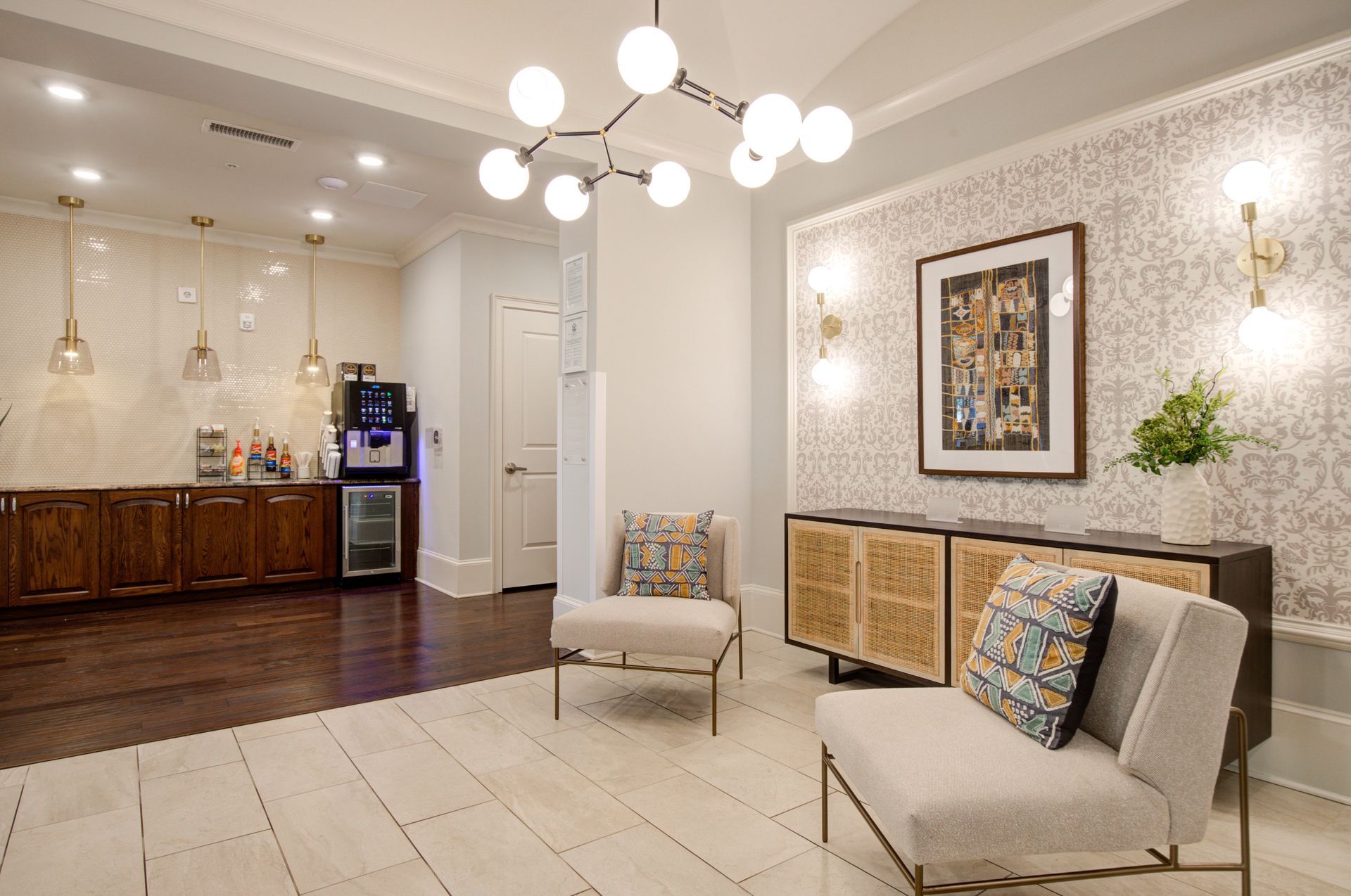 Lounge with chairs, buffet, and a coffee station, featuring wood, patterned wallpaper, and modern lighting.