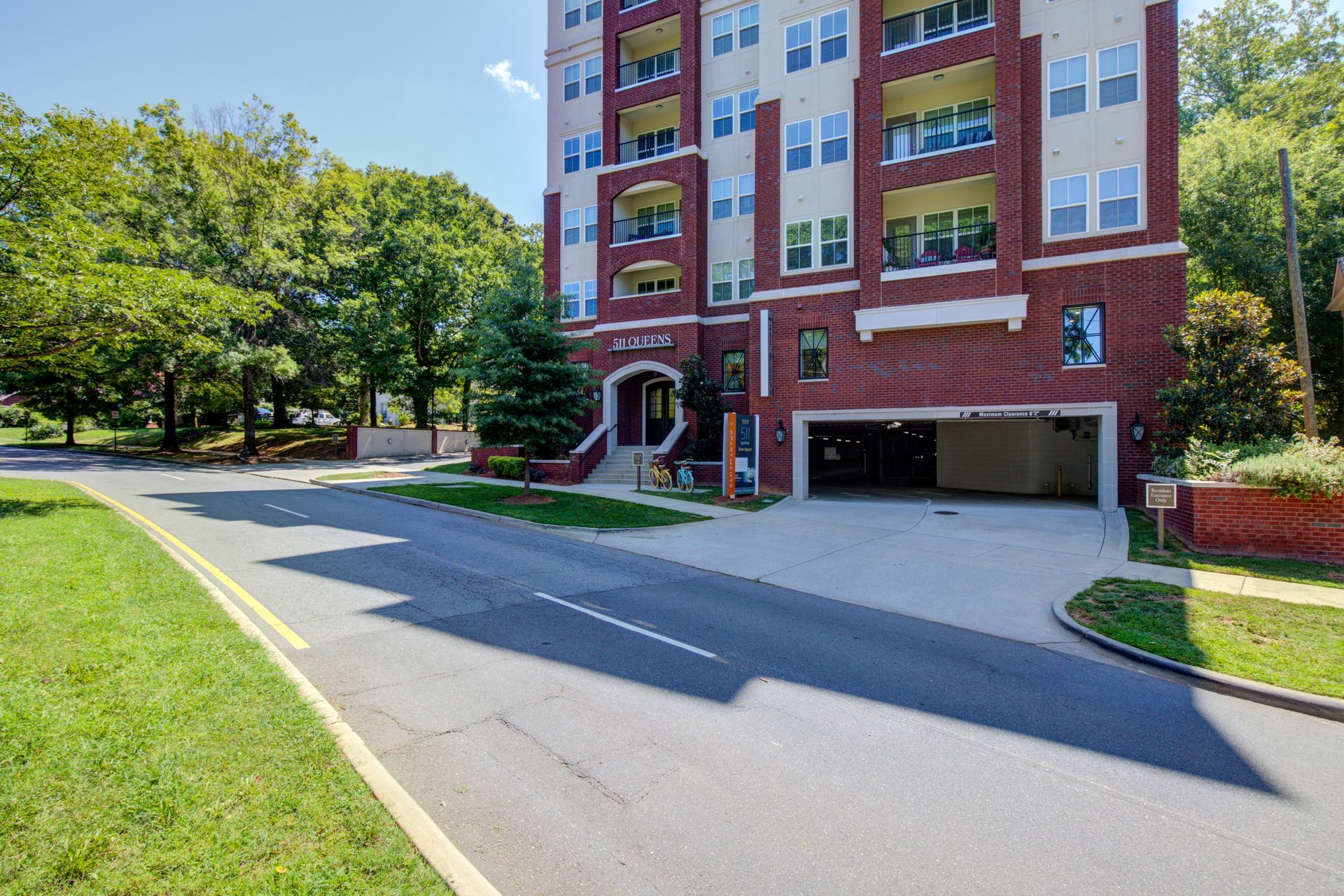 Apartment building with red brick facade, parking garage, and lush greenery.