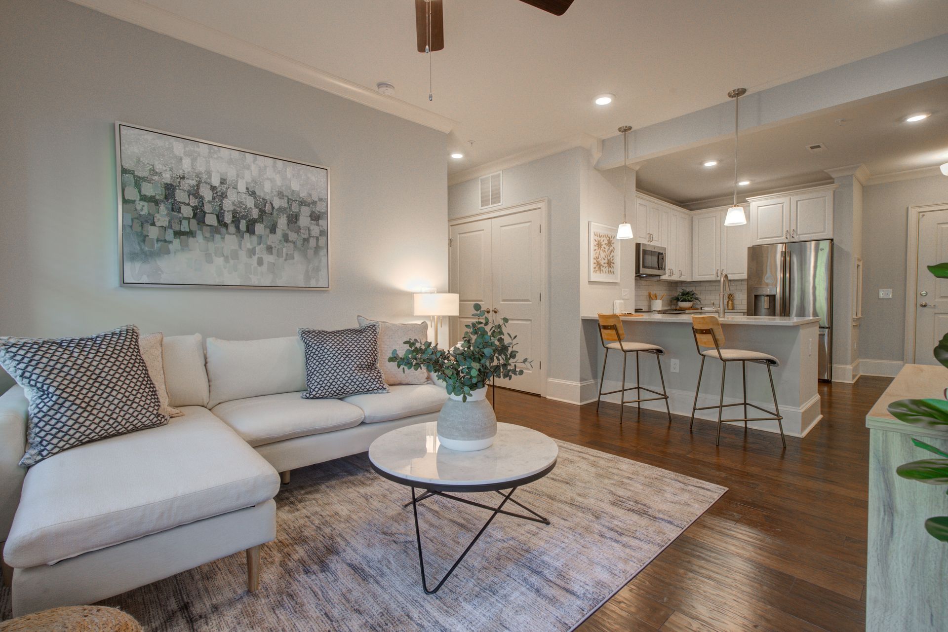 Living room with a sectional sofa, rug, and open kitchen. Light blue walls, hardwood floors.