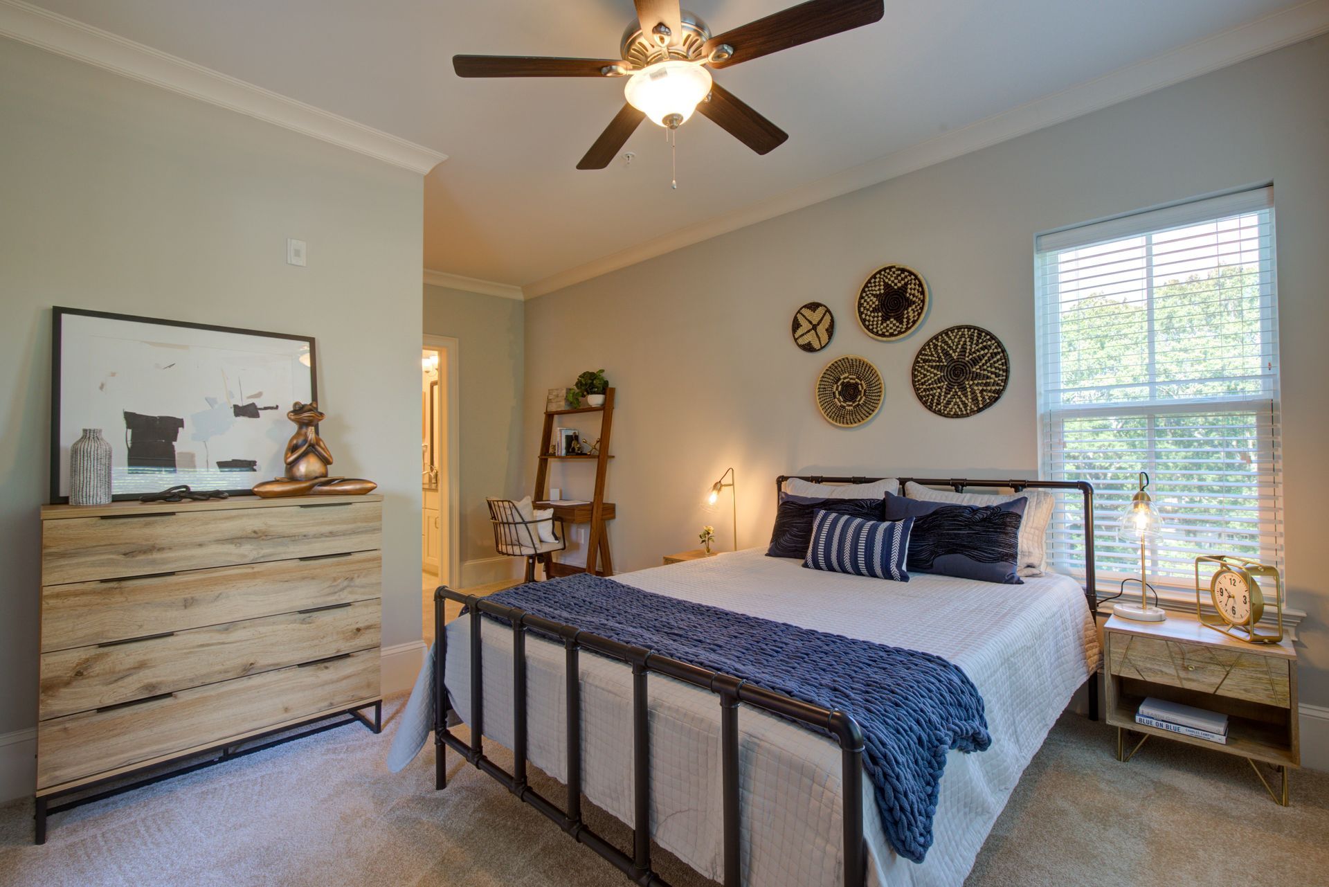 Bedroom with a metal bed frame, wooden dresser, and decorative wall art. Light blue walls and neutral carpet.
